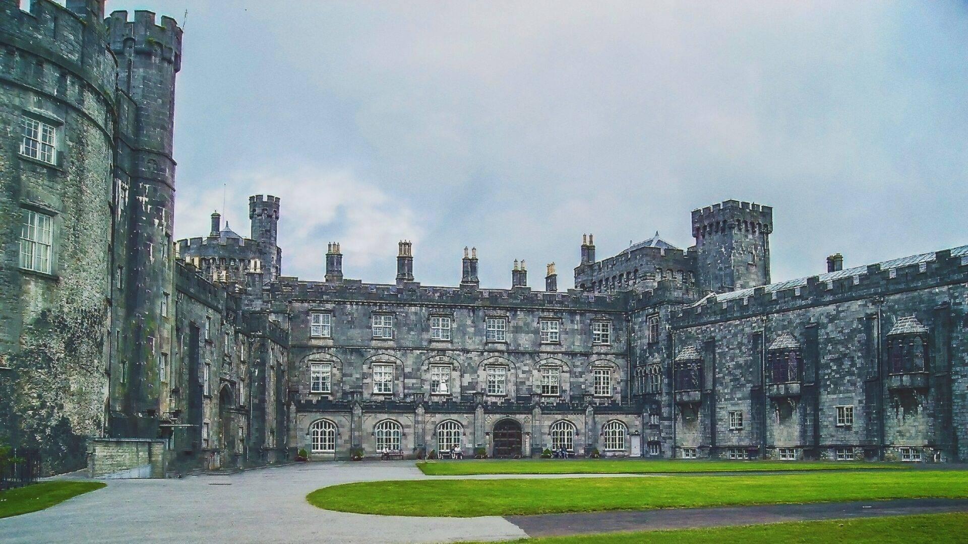 Une cour pavée entourée de bâtiments en pierre grise avec créneaux et tours caractéristiques d’une forteresse médiévale irlandaise