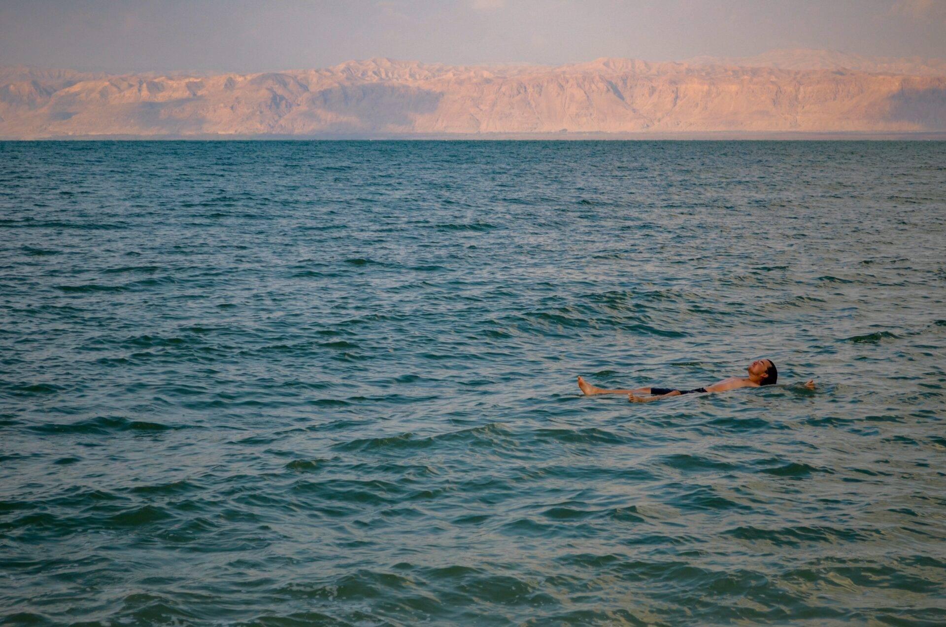 Un homme flotte sans effort dans une mer turquoise face à des falaises désertiques ocre majestueuses