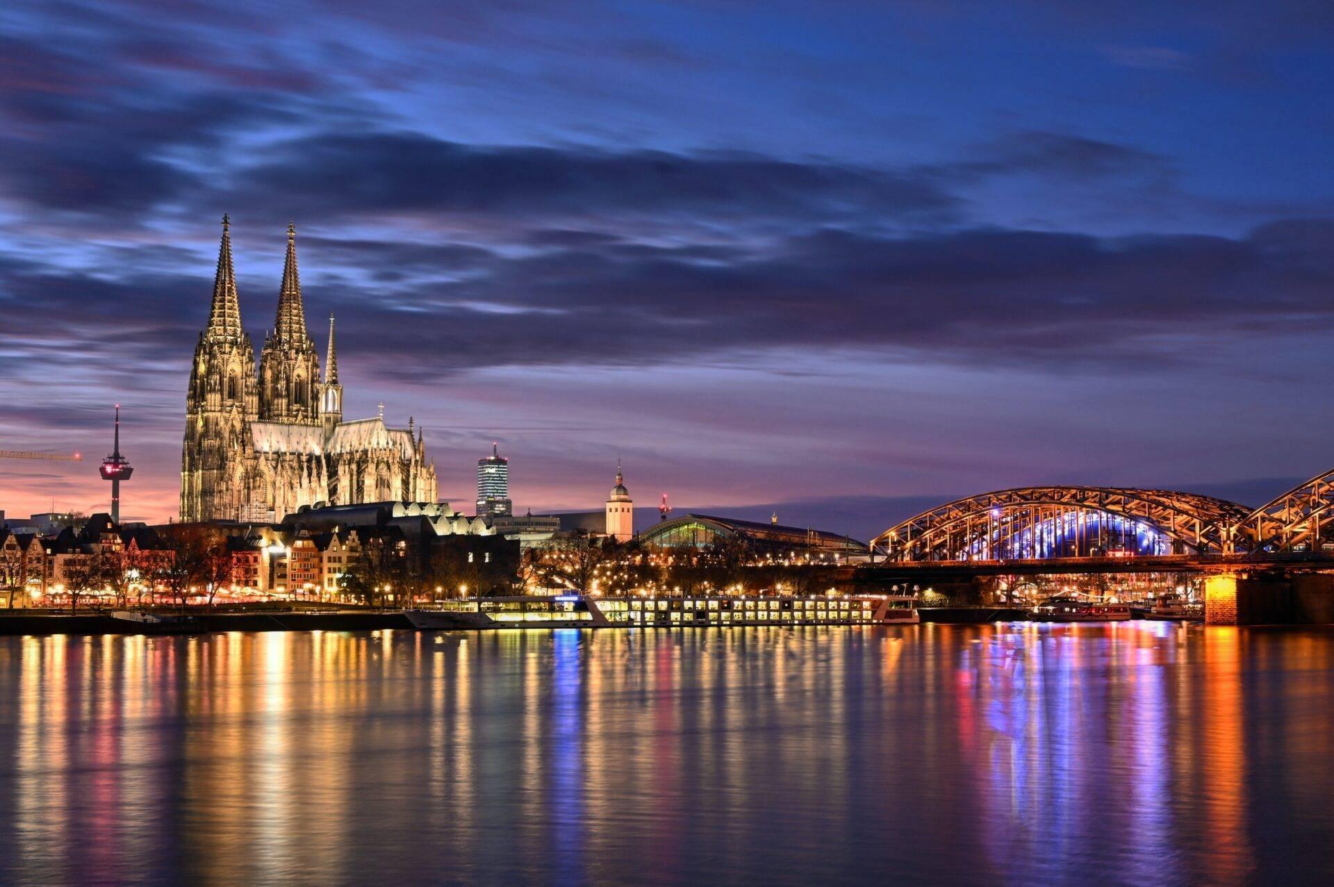 Cathédrale gothique illuminée au crépuscule avec pont métallique et reflets dans le fleuve en soirée