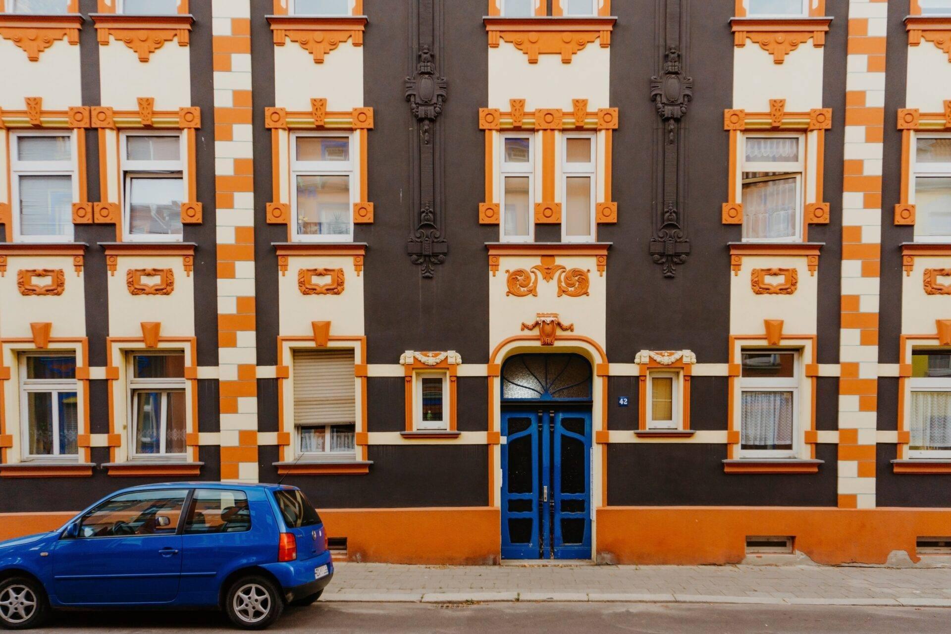 Façade colorée d’un bâtiment Art déco orange et noir avec voiture bleue garée devant