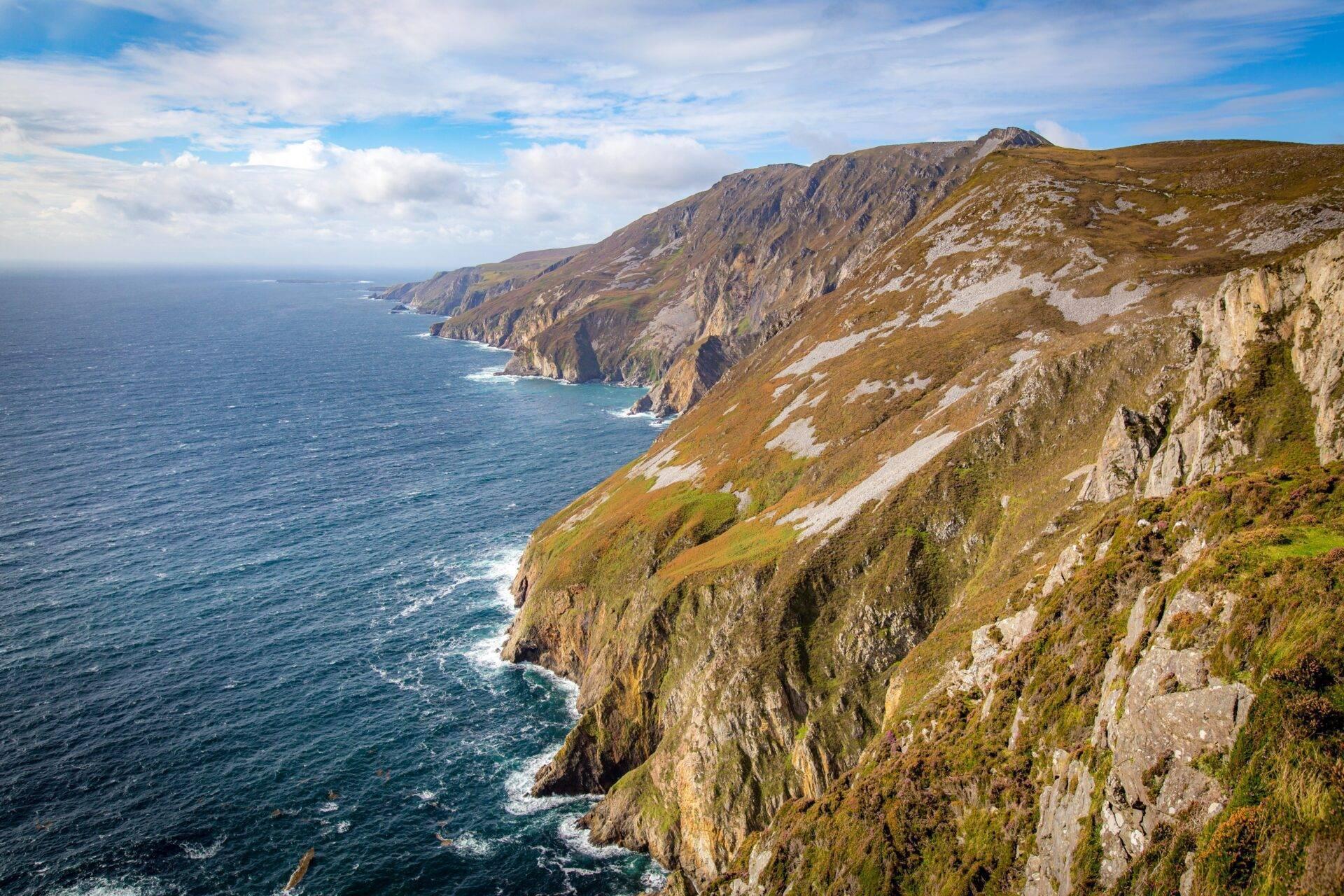Falaises côtières escarpées et verdoyantes surplombant l’océan Atlantique sous un ciel nuageux