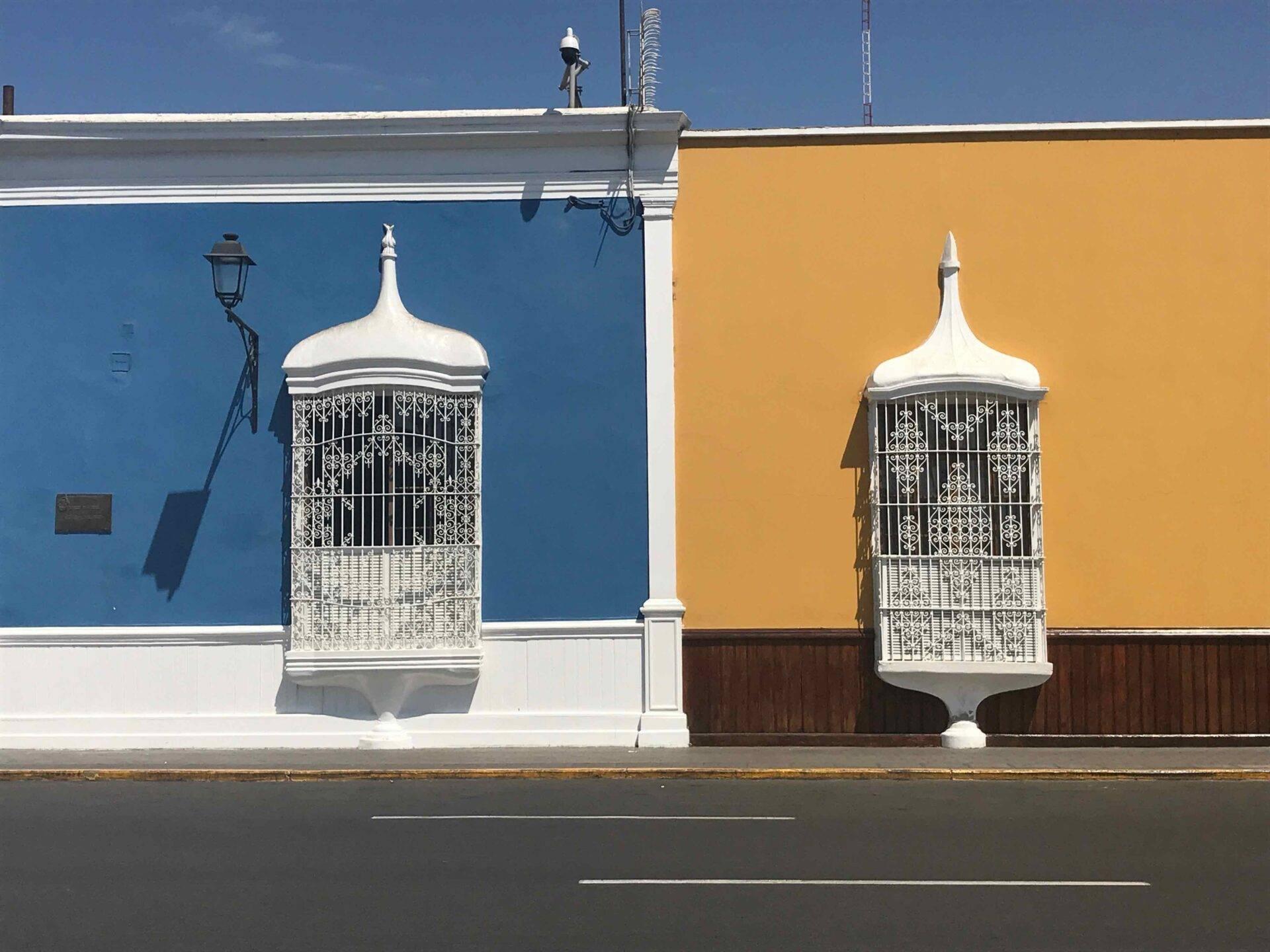 Deux cages à oiseaux blanches ornementales sur façades colorées bleue et jaune d’un bâtiment colonial