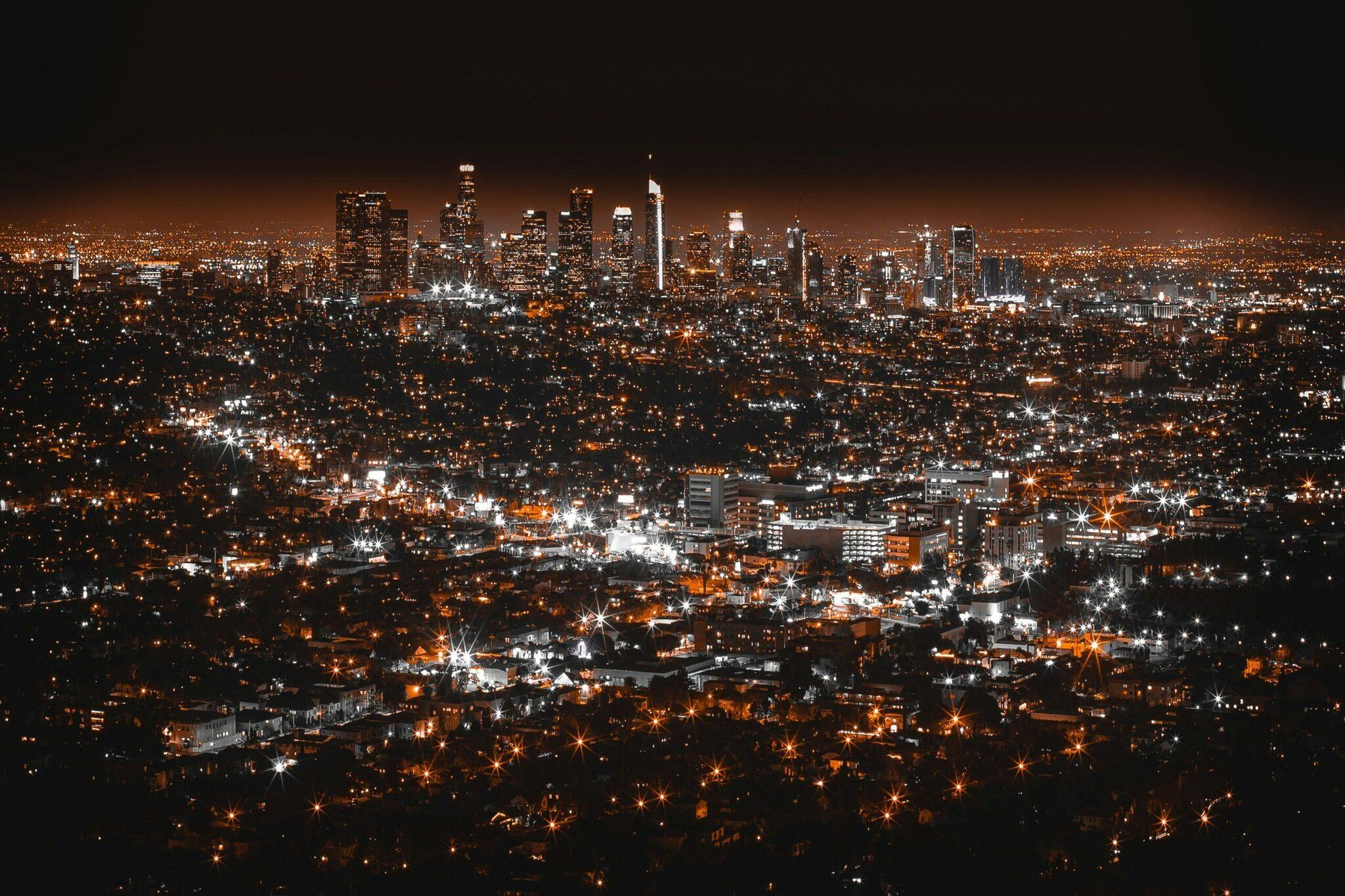 Vue nocturne d’une grande métropole avec gratte-ciel illuminés au centre et quartiers résidentiels scintillants s’étendant à l’horizon