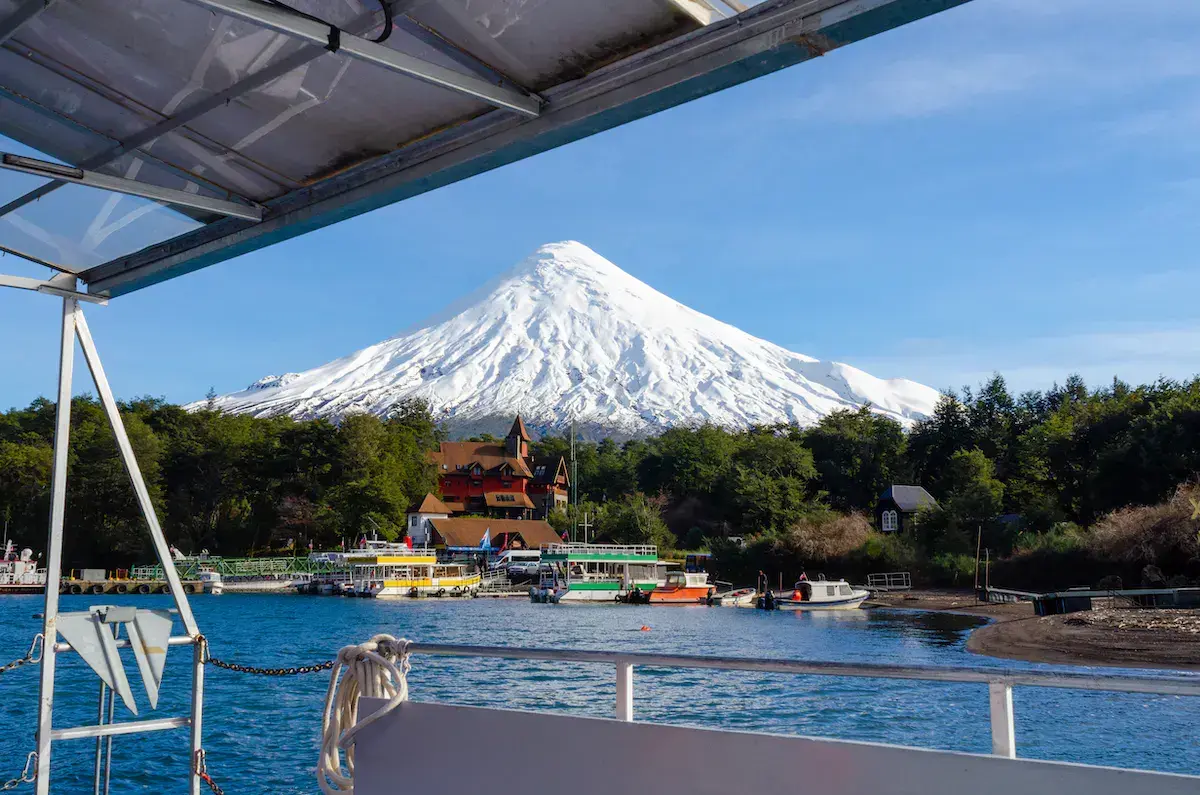 Vue depuis un bateau sur un volcan enneigé dominant un lac avec bâtiments colorés et embarcations