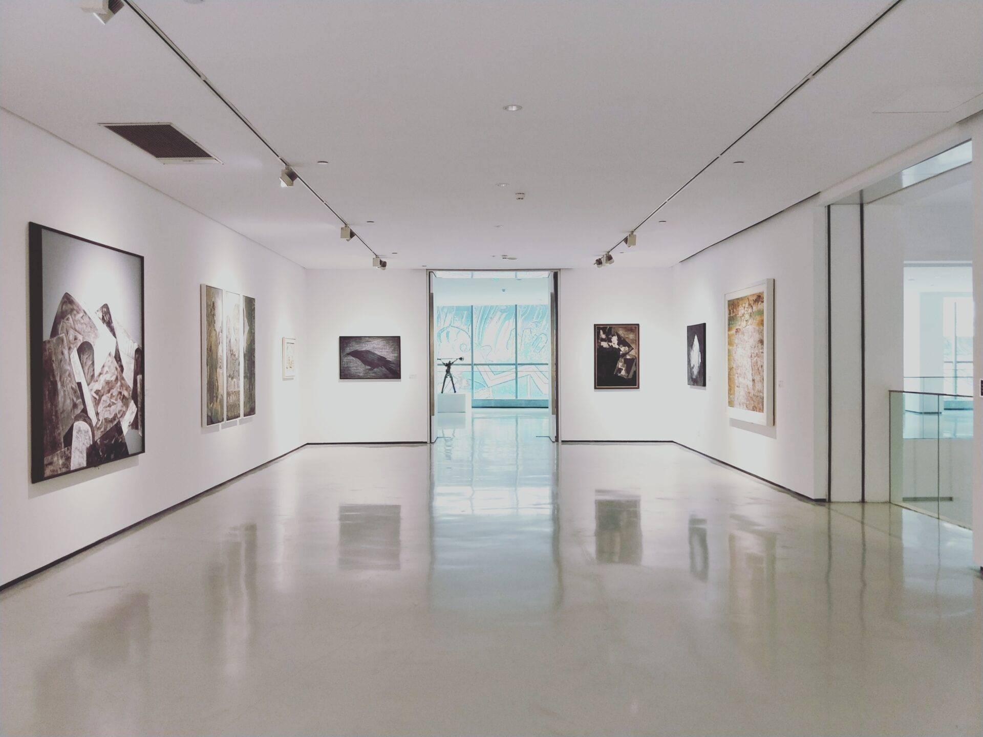 Galerie d’art contemporain épurée avec tableaux exposés sur murs blancs et sol brillant réfléchissant