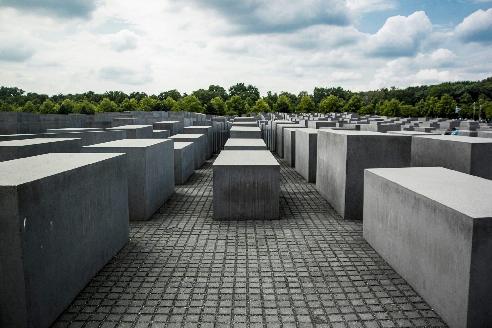Mémorial aux victimes de l’Holocauste avec ses blocs de béton gris alignés sous un ciel nuageux et forêt verdoyante