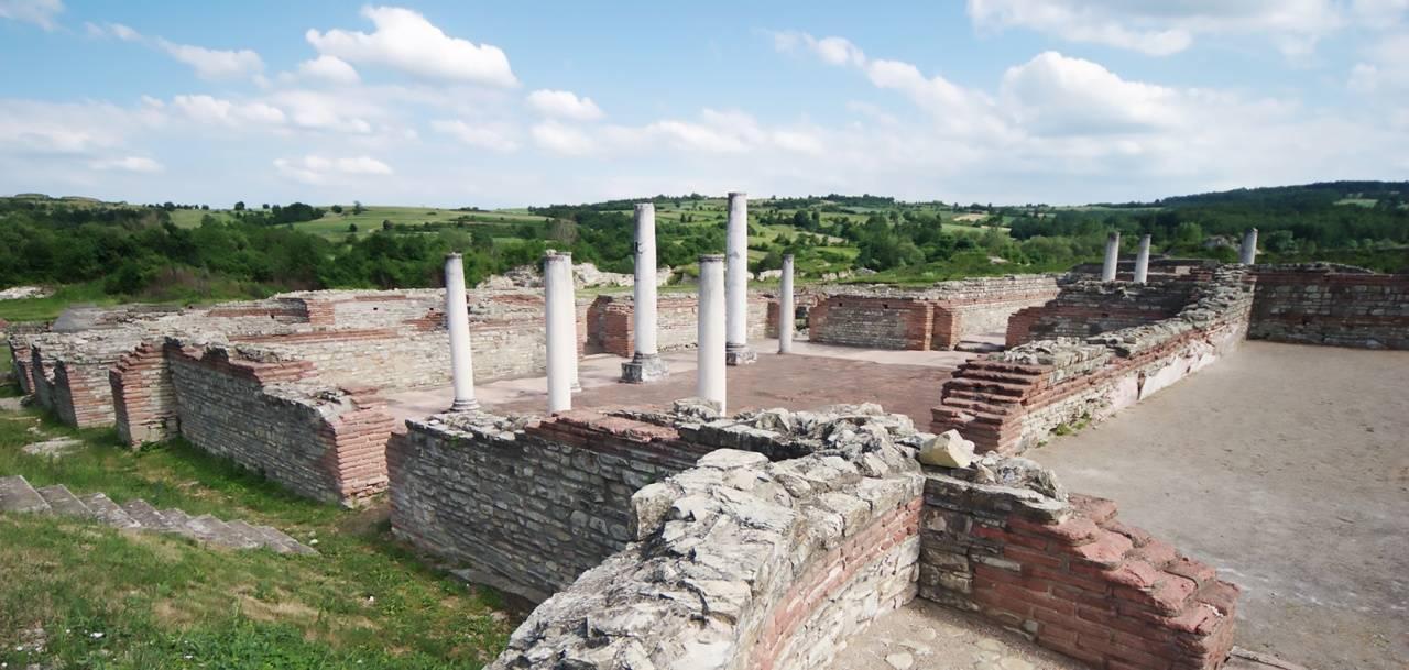 Ruines antiques avec colonnes blanches reconstituées et murs en briques rouges dans un paysage verdoyant