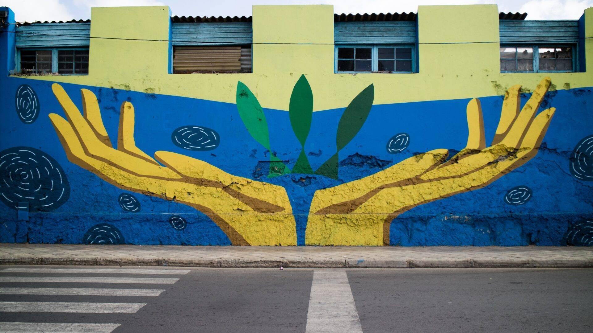 Fresque murale colorée représentant des mains jaunes protégeant une plante verte sur fond bleu