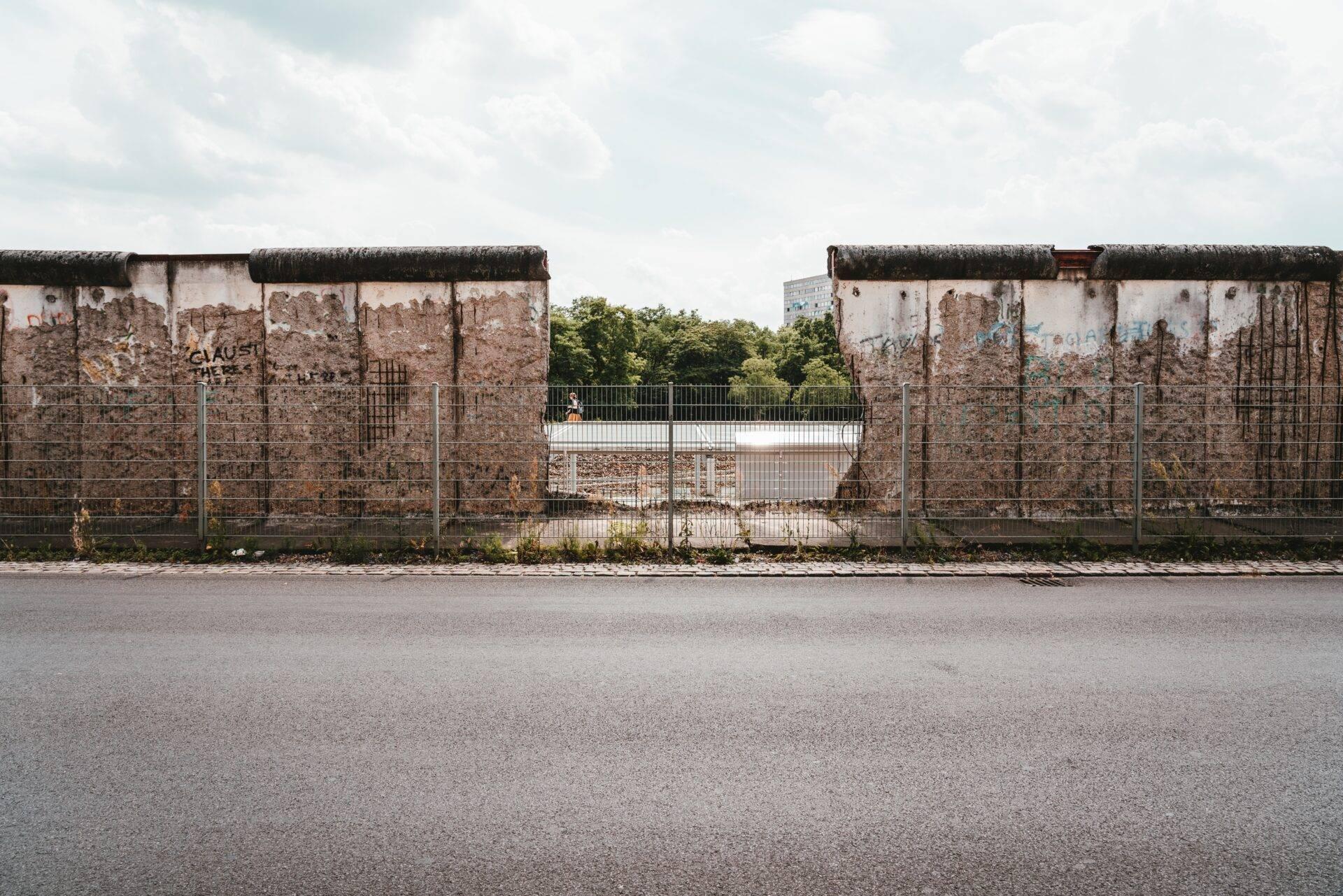 Vestiges du Mur de Berlin avec briques apparentes, graffitis et clôture métallique, par jour nuageux