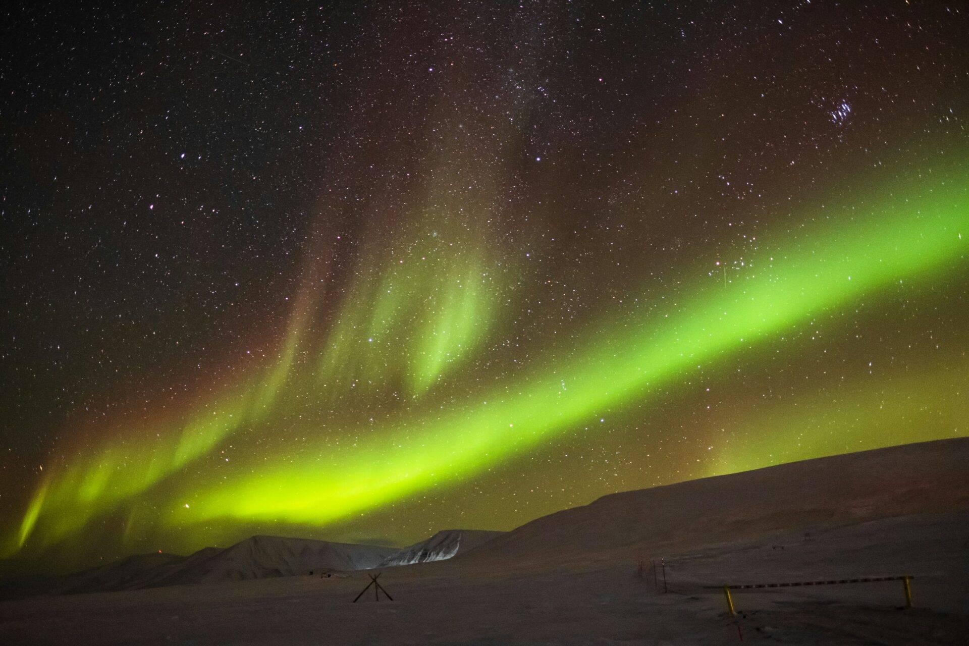 Aurores boréales vertes dansant au-dessus d’un paysage enneigé arctique parsemé d’équipements