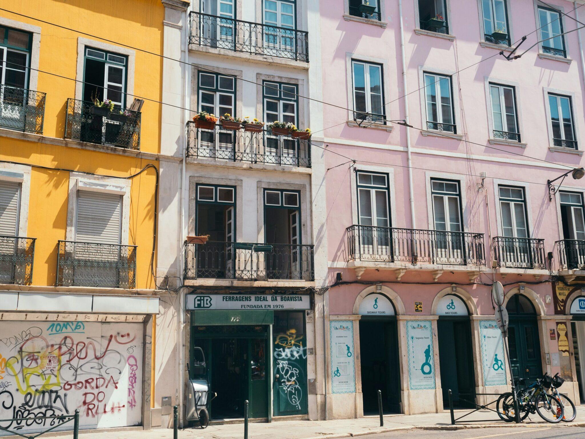 Façades colorées jaune, blanche et rose d’immeubles anciens lisboètes avec commerces au rez-de-chaussée et balcons ornementés