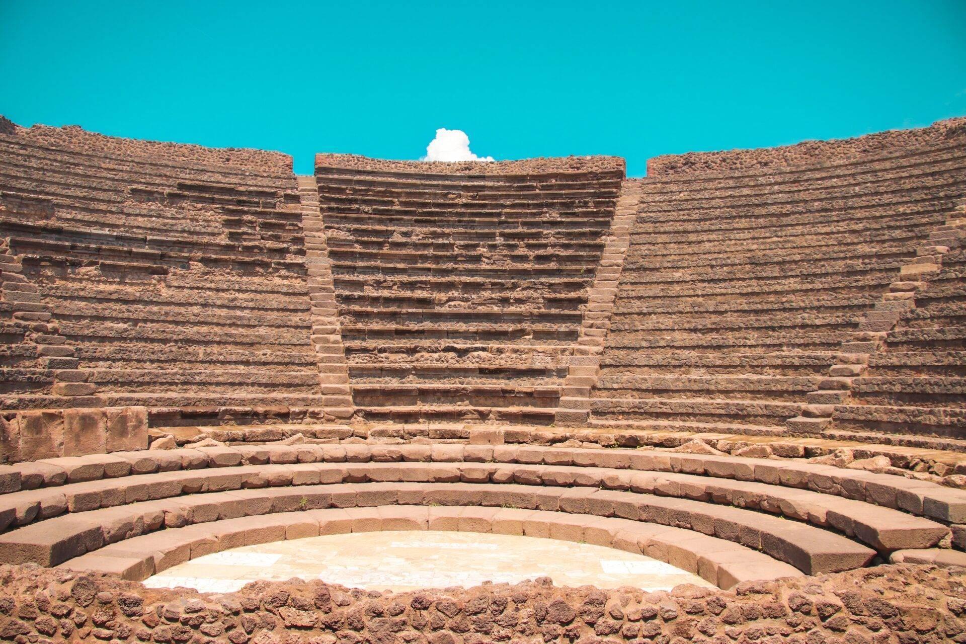 Amphithéâtre antique en ruines avec gradins de pierre concentriques et ciel bleu dégagé