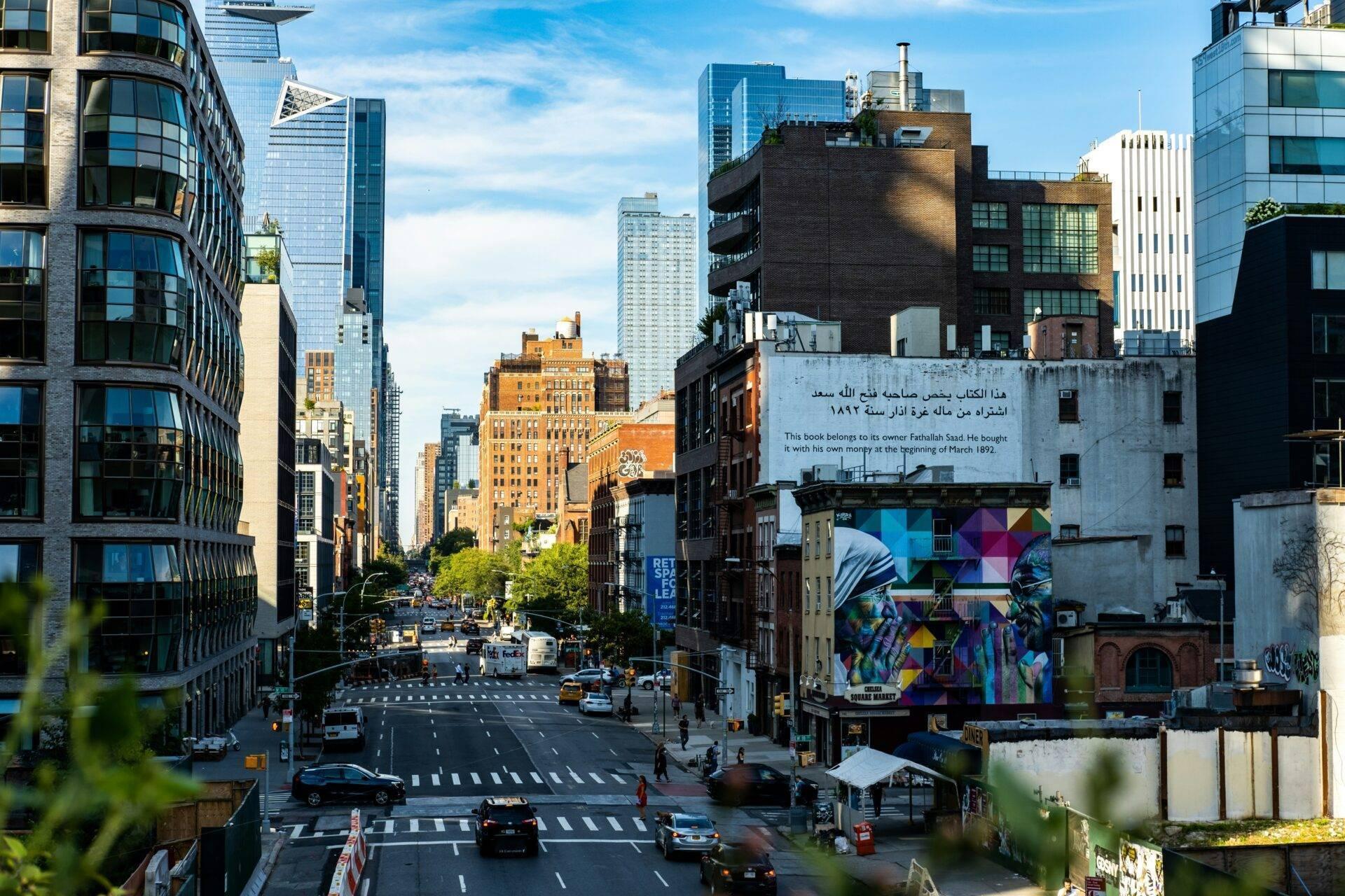 Vue d’une avenue urbaine animée avec immeubles modernes et historiques, carrefour avec circulation, street art coloré et ciel dégagé