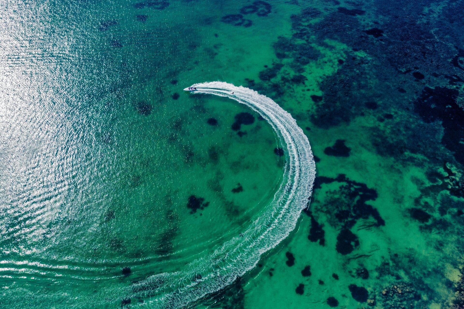 Un bateau à moteur traçant un sillage blanc circulaire dans une eau turquoise cristalline parsemée de rochers noirs