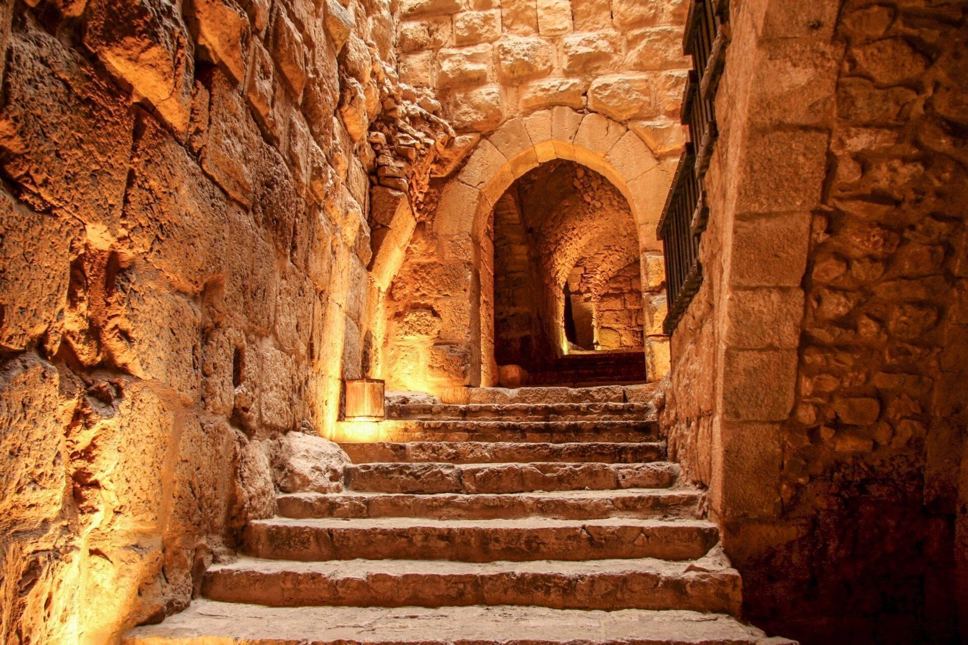 Escalier en pierre illuminé menant à une arche voûtée dans une ancienne forteresse ou citadelle du Moyen-Orient