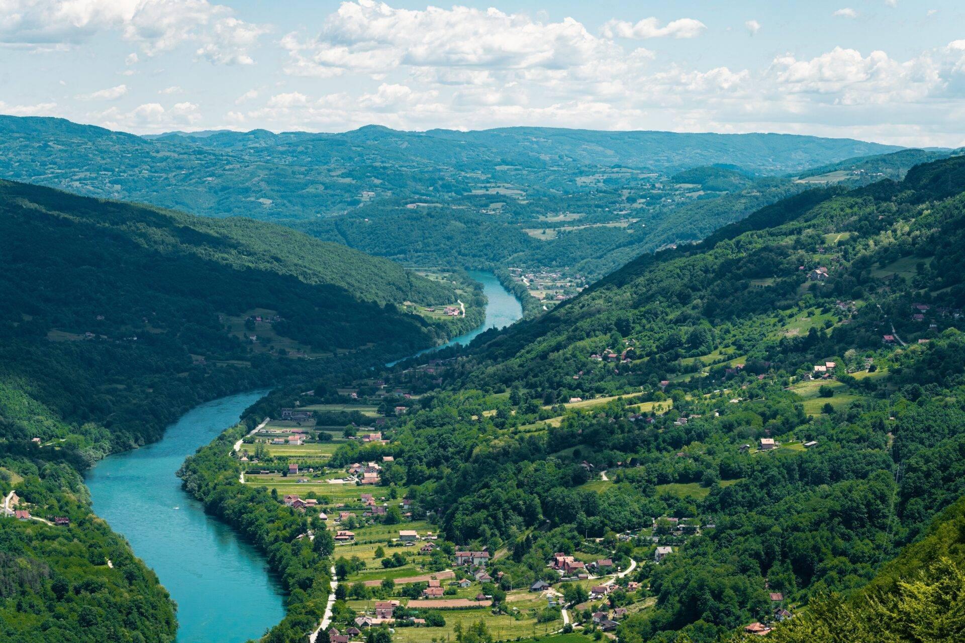 Une vallée fluviale verdoyante traversée par une rivière turquoise, entourée de montagnes boisées et de petits villages