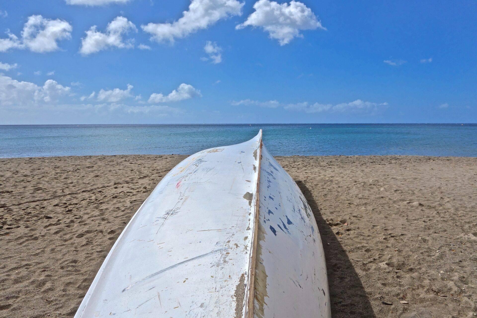Un vieux bateau blanc échoué sur une plage de sable fin face à une mer turquoise sous un ciel bleu