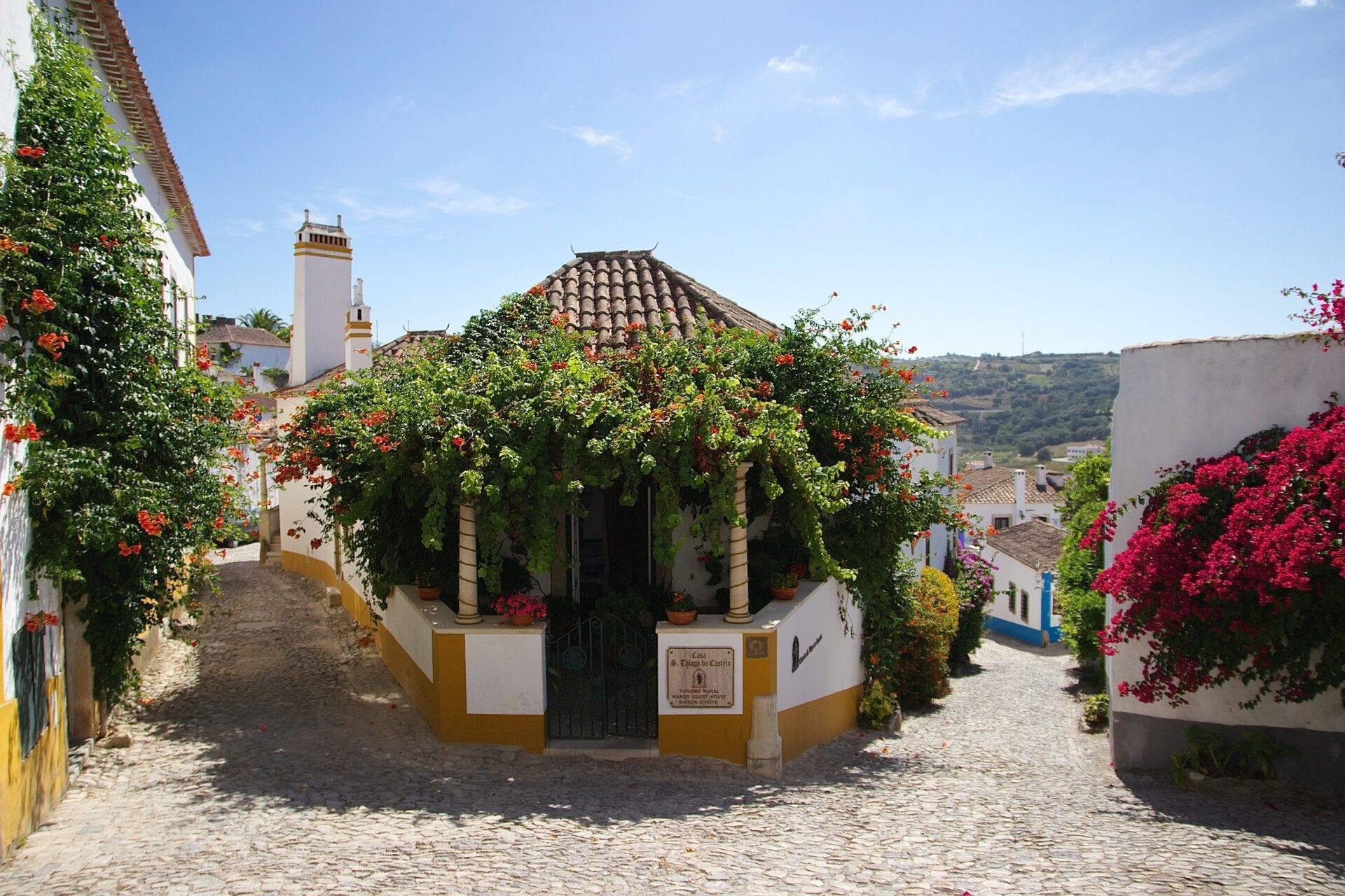 Une ruelle pavée pittoresque avec une chapelle blanche et jaune entourée de fleurs rouges vives