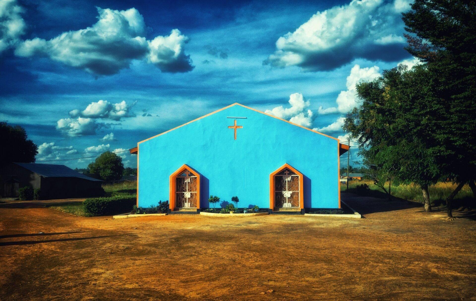 Une église aux murs bleu vif et portes orange dans une savane africaine sous un ciel nuageux