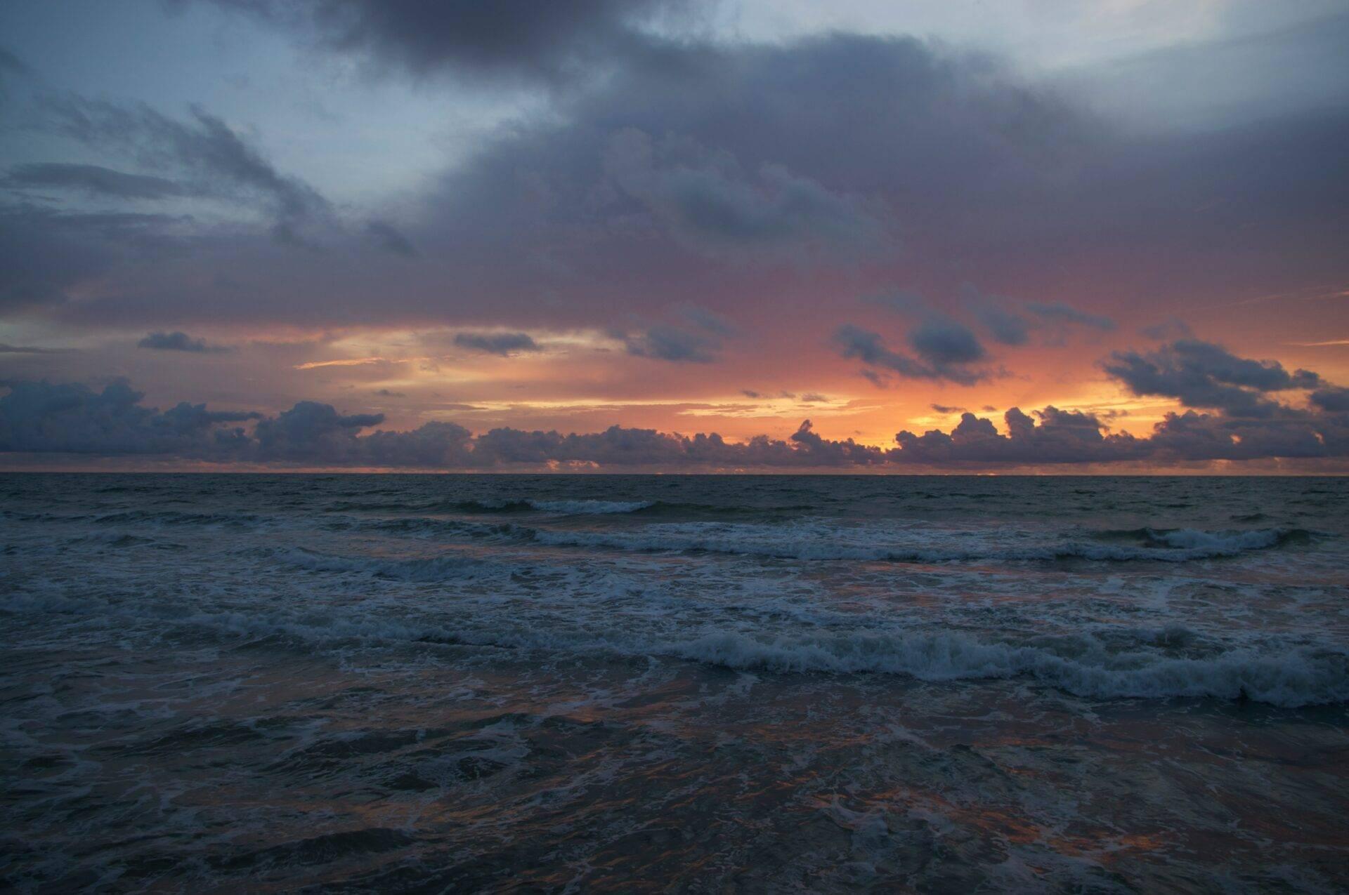 Coucher de soleil spectaculaire sur l’océan avec nuages dorés et vagues sur une plage déserte