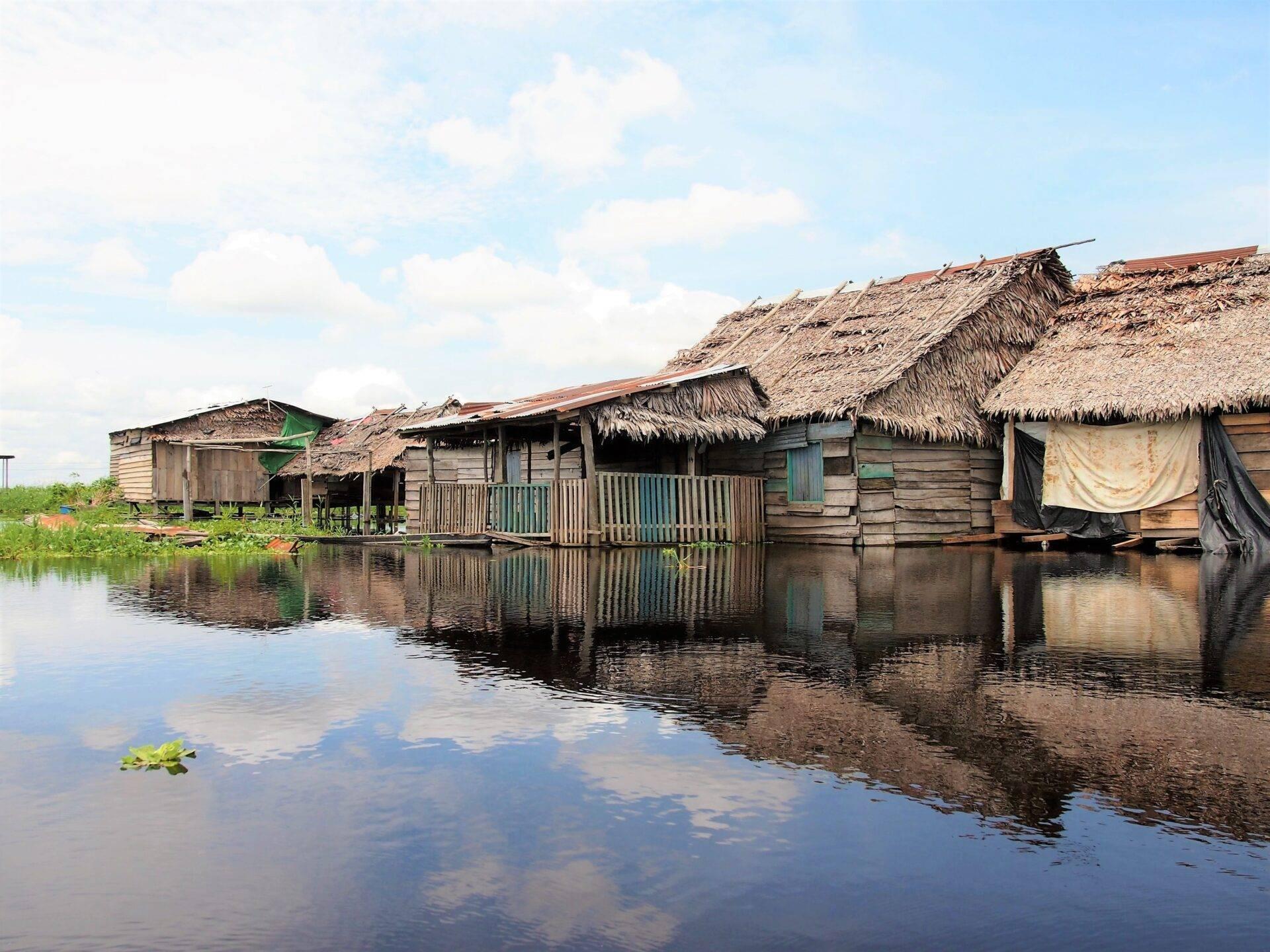 Des habitations sur pilotis avec toits de chaume bordent un canal d’eau calme en Amazonie