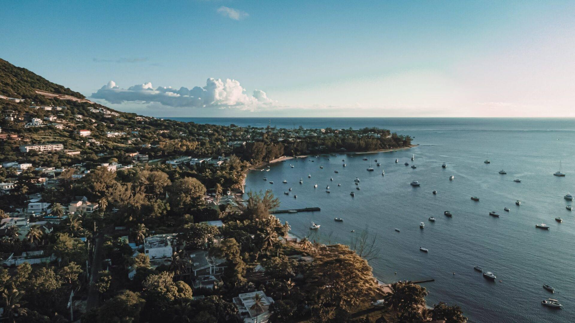 Une baie côtière tropicale avec maisons éparpillées sur les collines boisées, voiliers ancrés et ciel dégagé