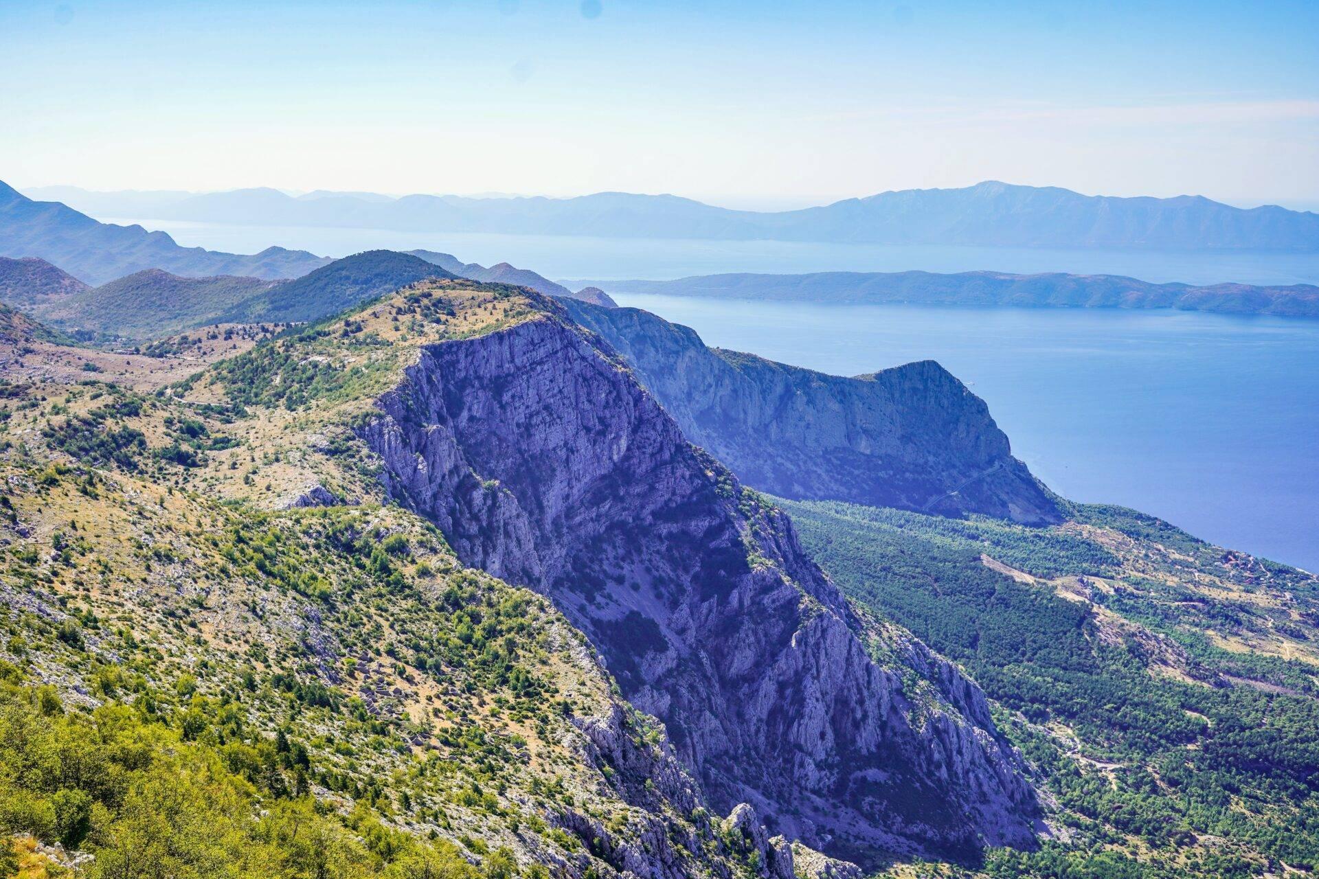 Vue panoramique sur des montagnes calcaires abruptes surplombant une mer Méditerranée turquoise et des îles lointaines