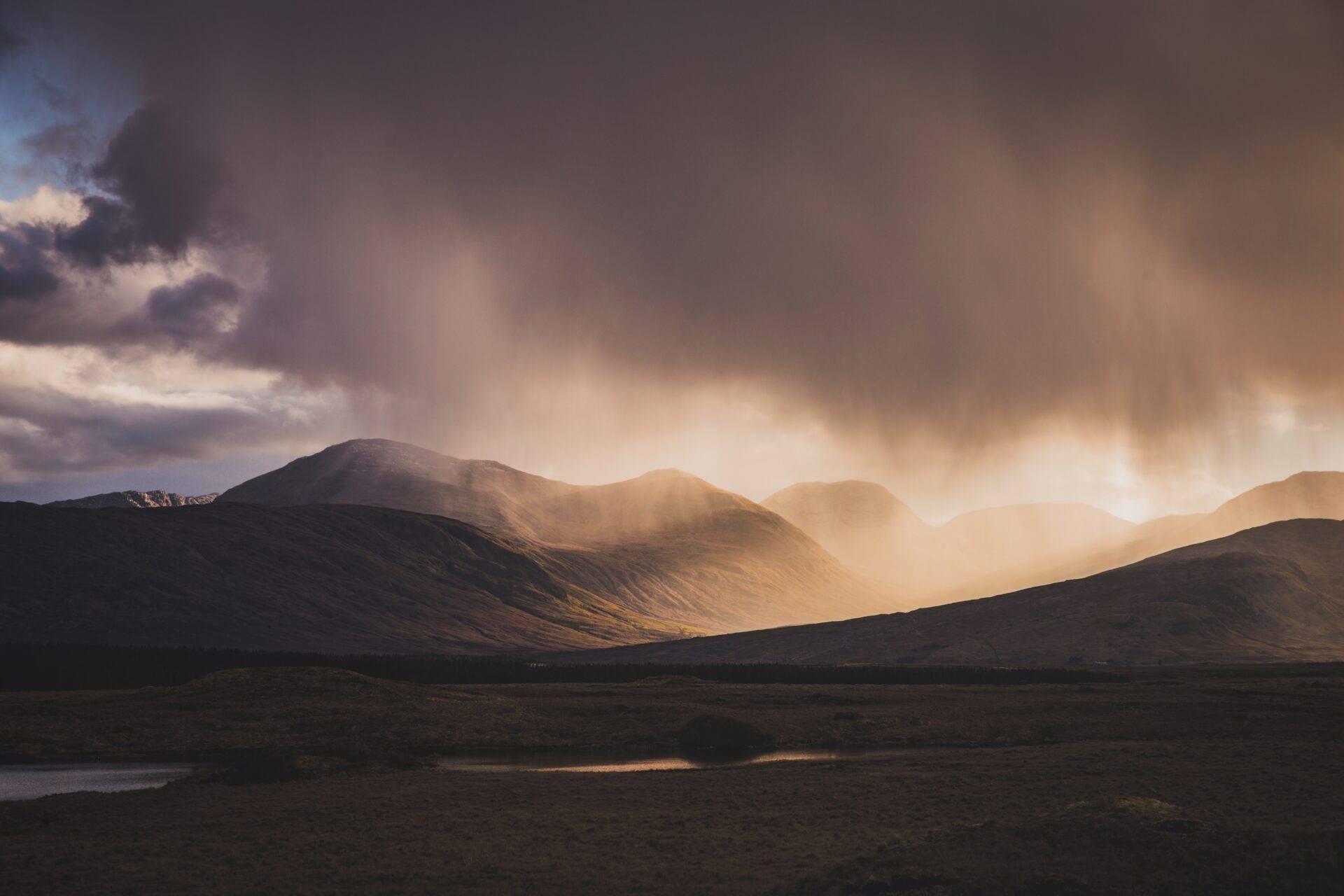 Montagnes arides baignées de lumière dorée avec un ciel nuageux dramatique et une rivière en contrebas