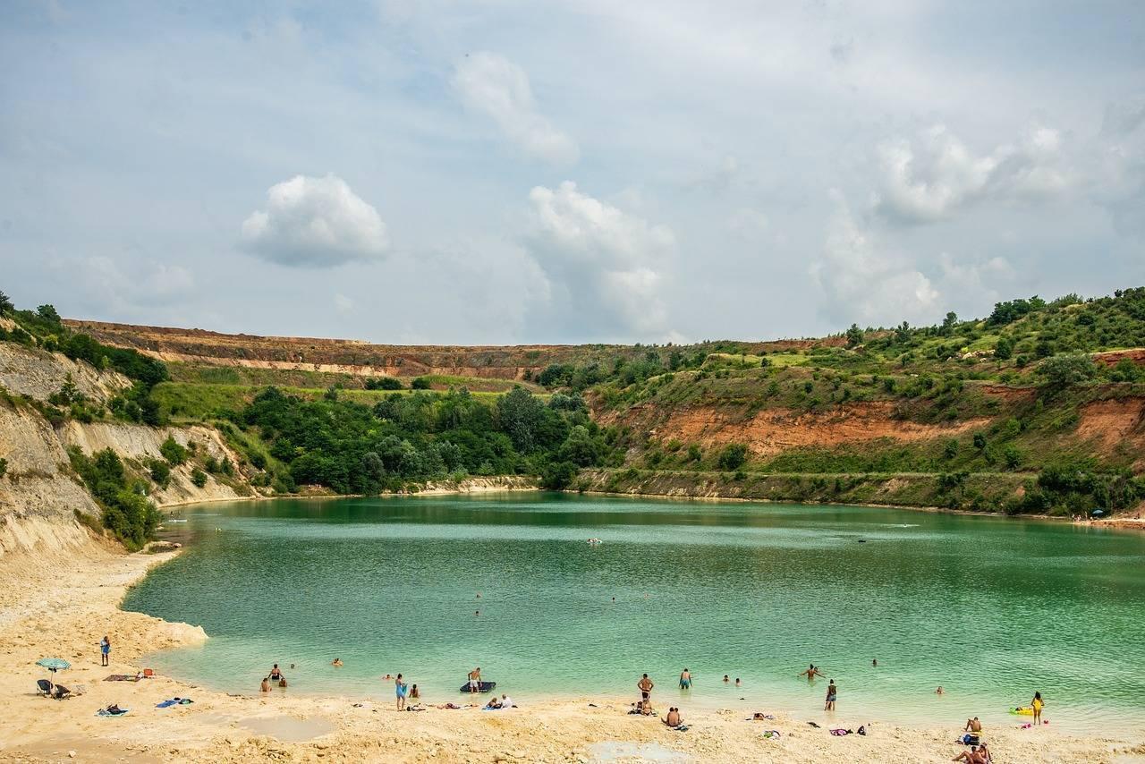 Un lac turquoise entouré de falaises verdoyantes avec baigneurs sur une plage de sable blanc
