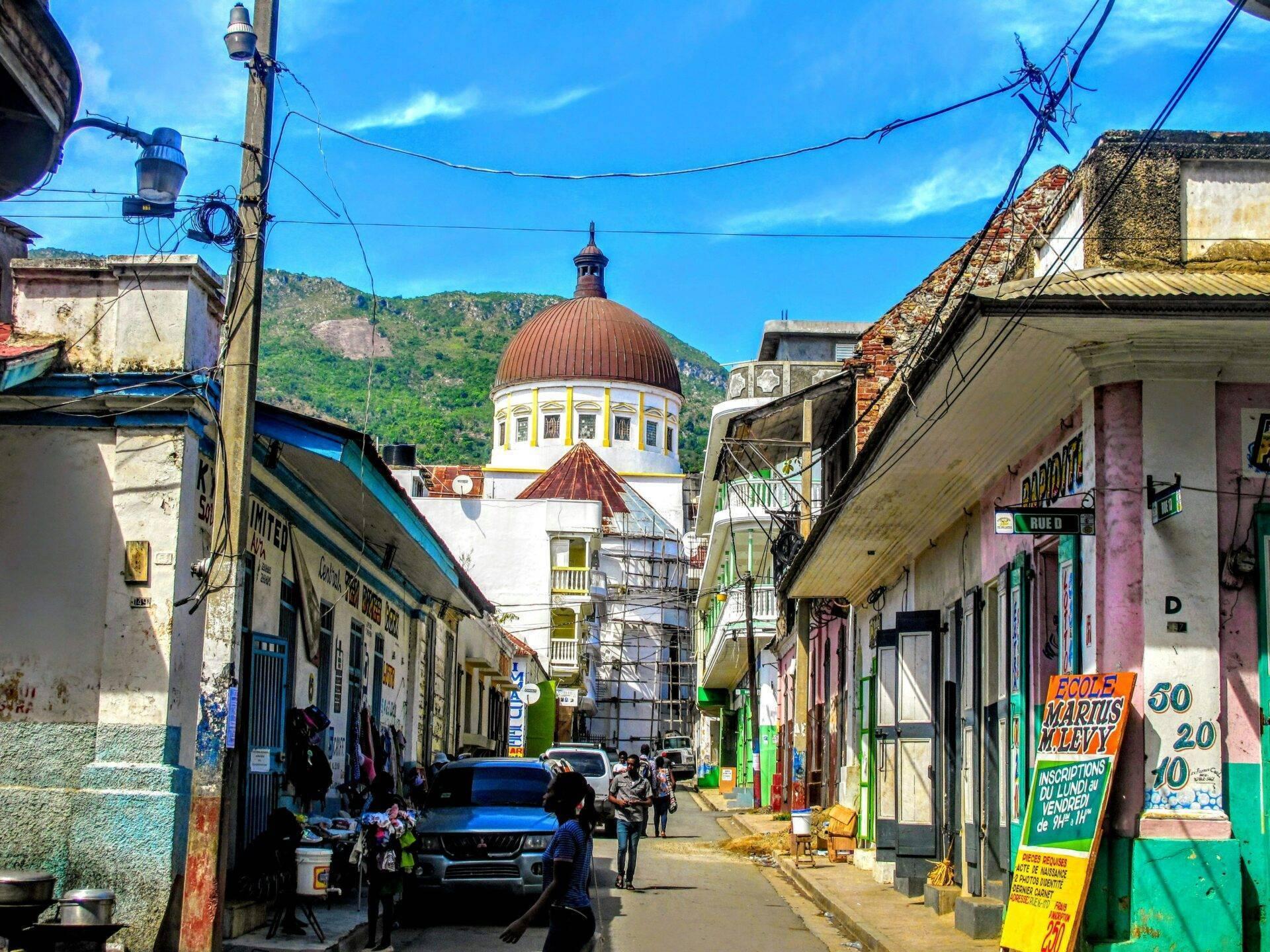 Une rue colorée d’une ville caribéenne avec une église à dôme rouge dominant l’horizon montagneux