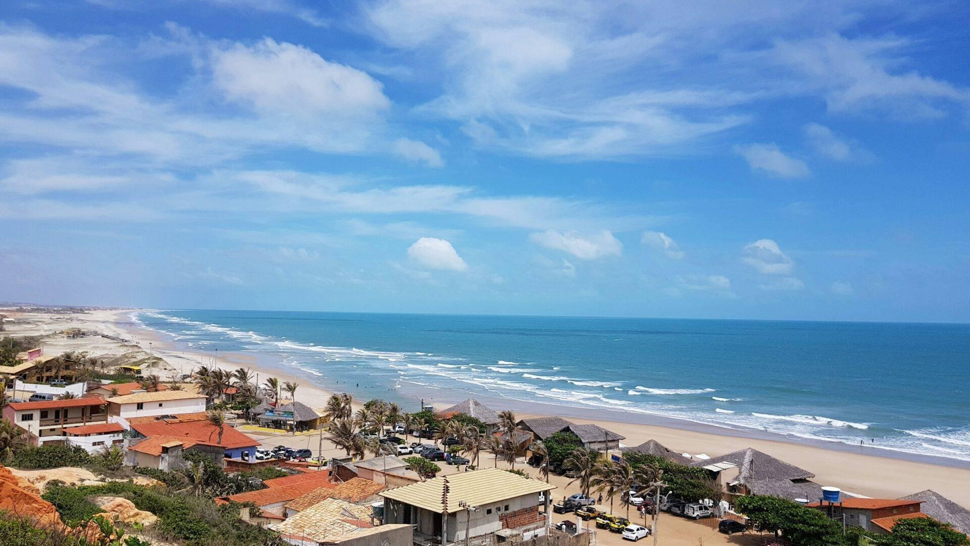 Vue aérienne d’une plage de sable blanc avec des vagues, des maisons colorées à toits oranges et des palmiers