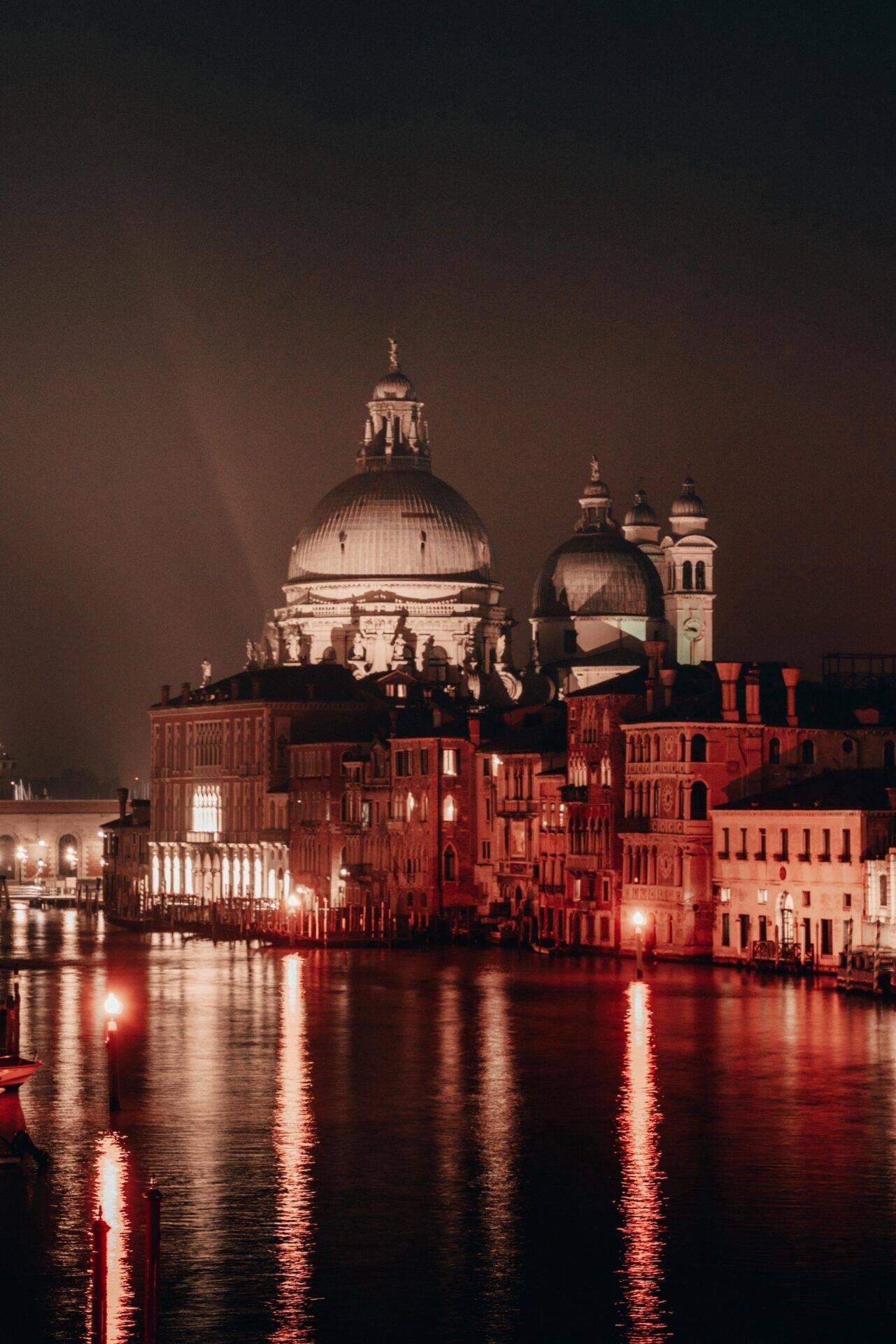 Vue nocturne de la Basilique de la Salute illuminée au-dessus du Grand Canal avec ses bâtiments historiques en briques rouges