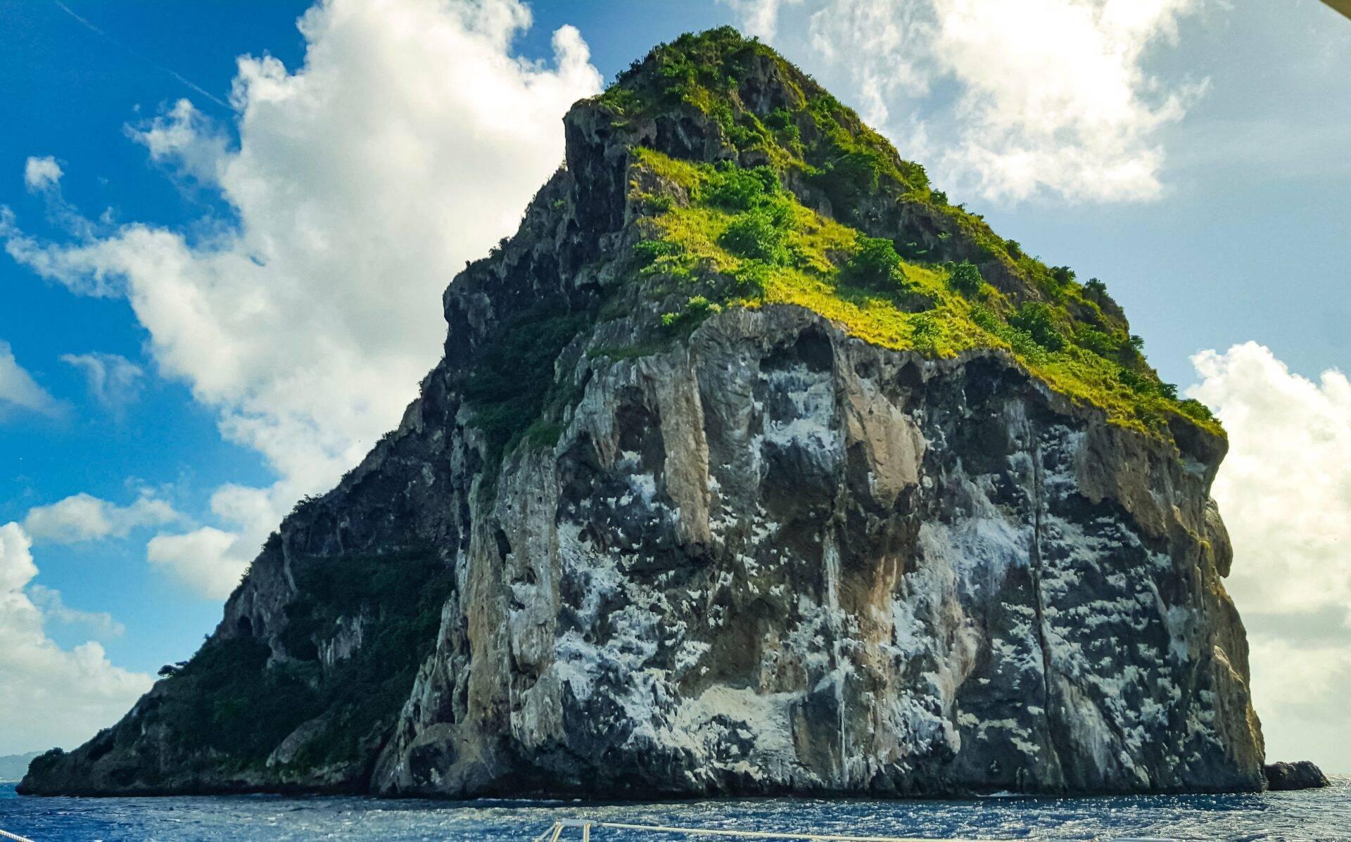 Un rocher calcaire escarpé couvert de végétation émerge de la mer turquoise sous un ciel bleu dégagé
