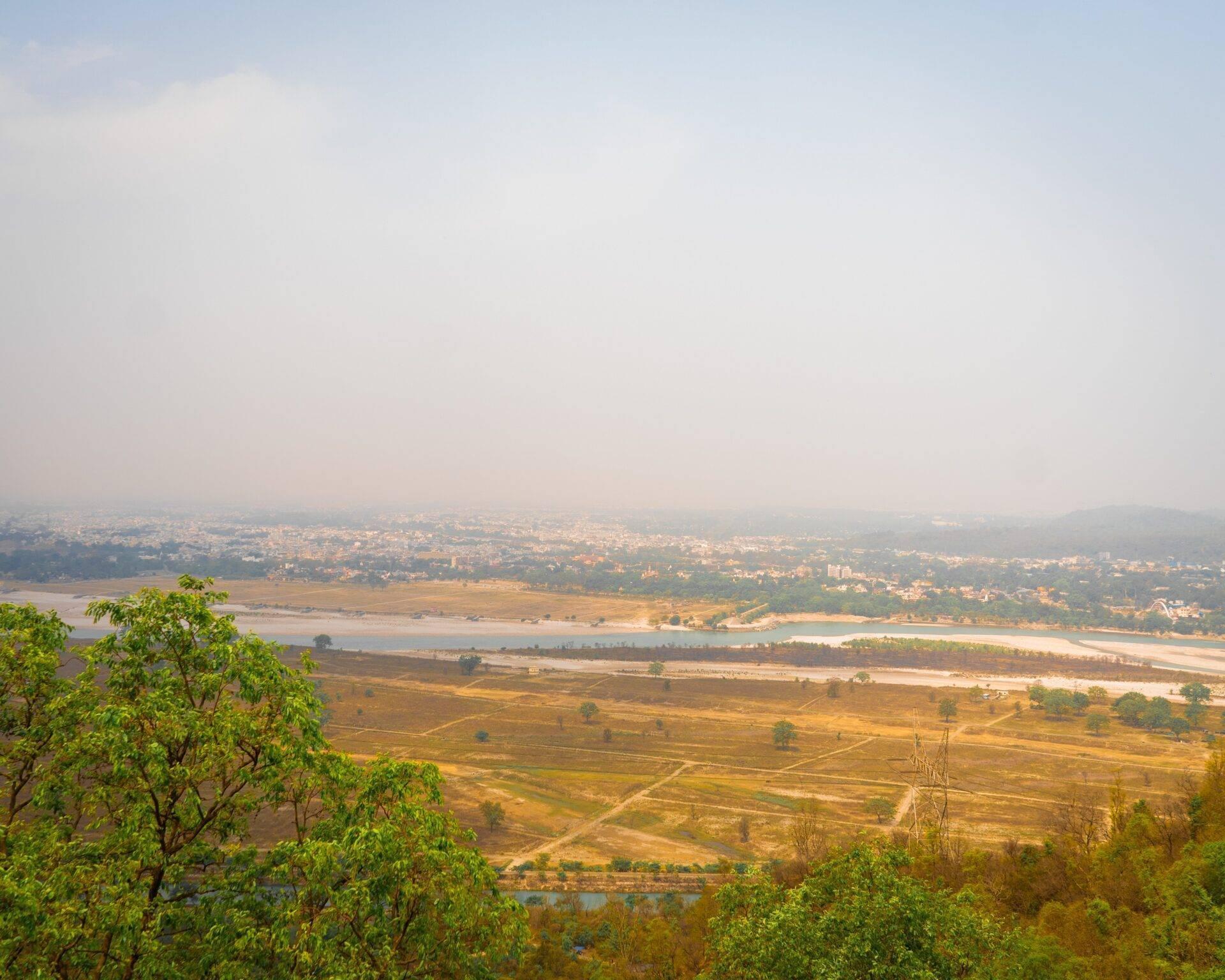 Vue panoramique d’une vallée fluviale avec rizières, villages dispersés et brume atmosphérique en arrière-plan