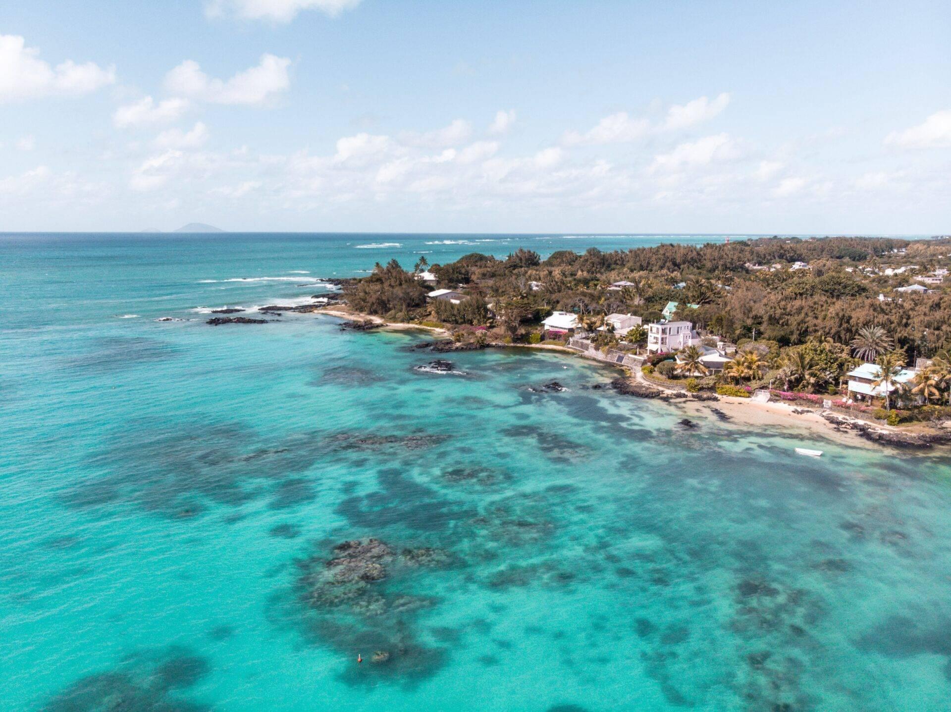 Vue aérienne d’une baie turquoise avec plages, maisons côtières et végétation tropicale