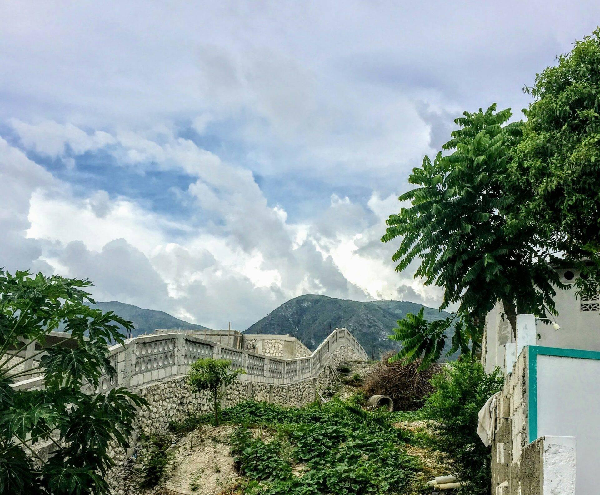 Vue sur des ruines de fortification en pierre avec montagnes boisées en arrière-plan sous ciel nuageux
