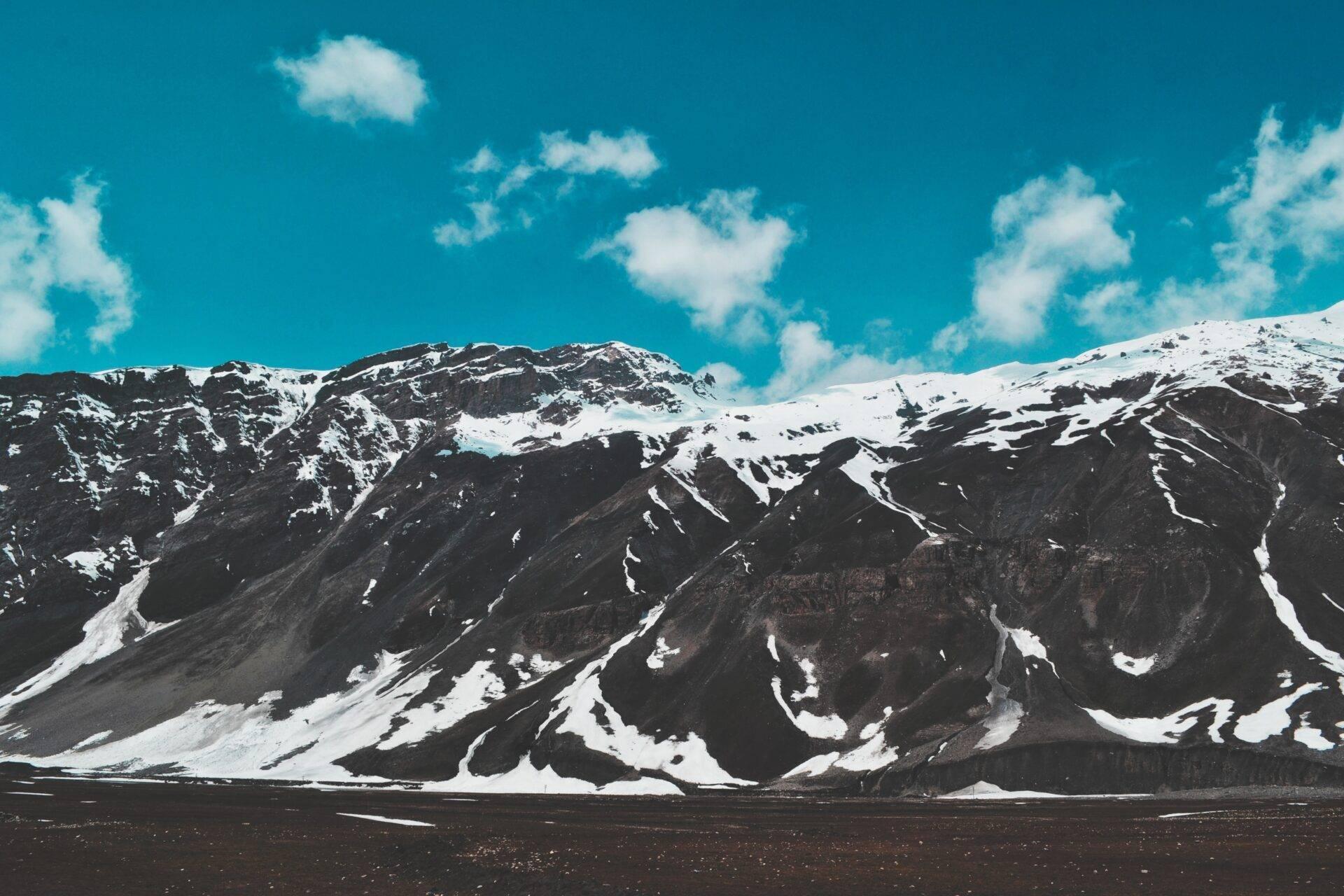 Chaîne de montagnes enneigées avec pentes rocheuses noires et ciel bleu dégagé, paysage désertique alpin spectaculaire