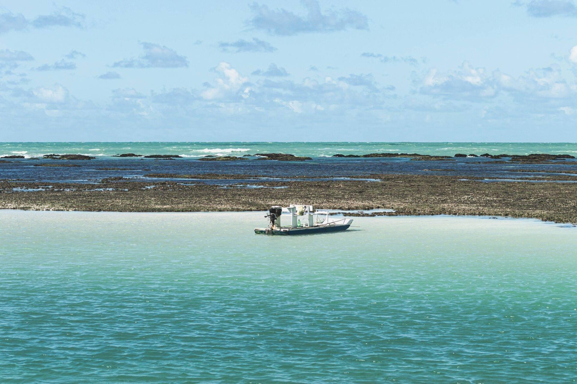 Un petit bateau de pêche blanc ancré dans les eaux turquoise peu profondes près d’une plage rocheuse