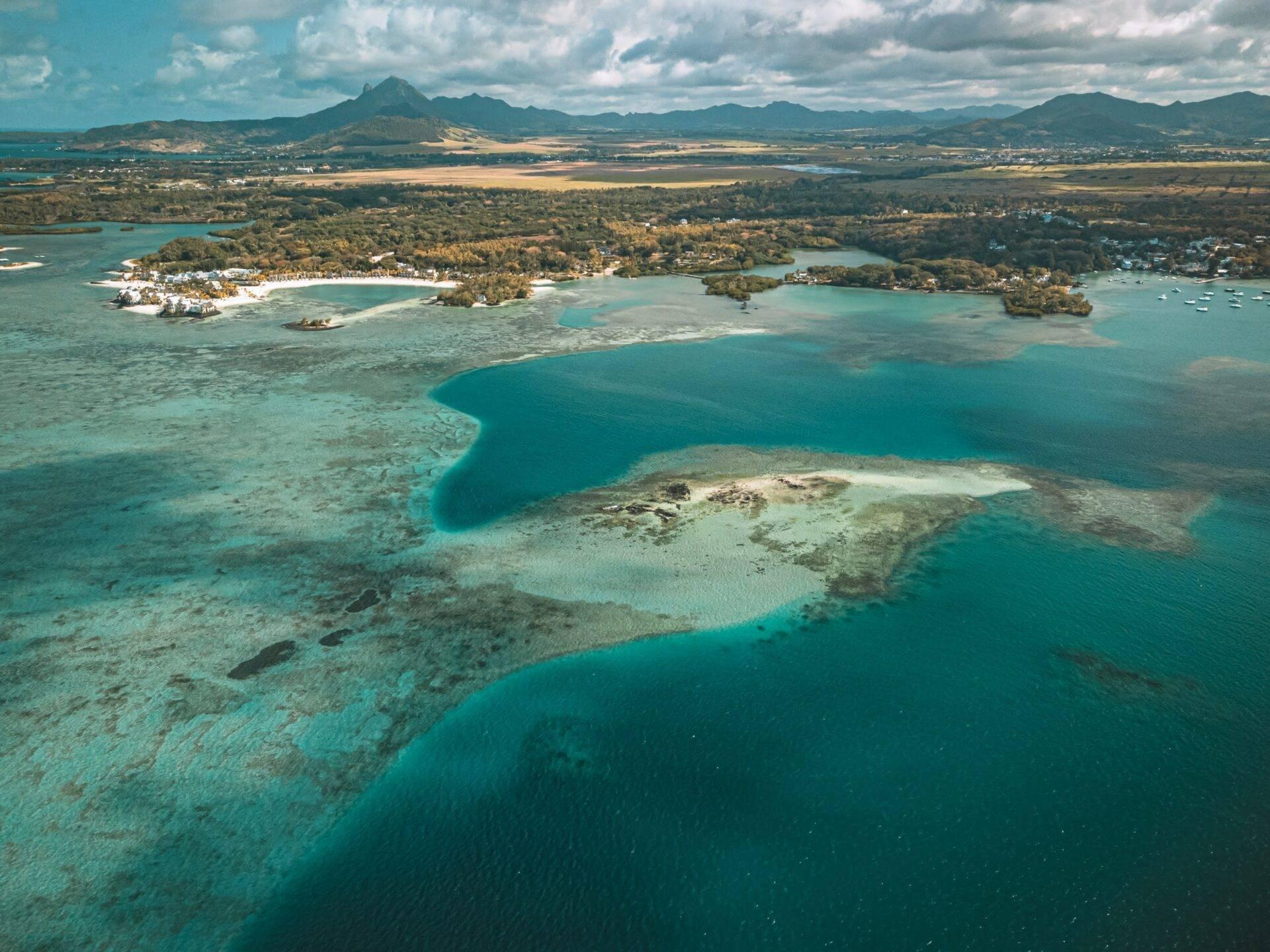 Vue aérienne d’une baie turquoise avec îlots boisés, plages blanches et montagnes verdoyantes en arrière-plan