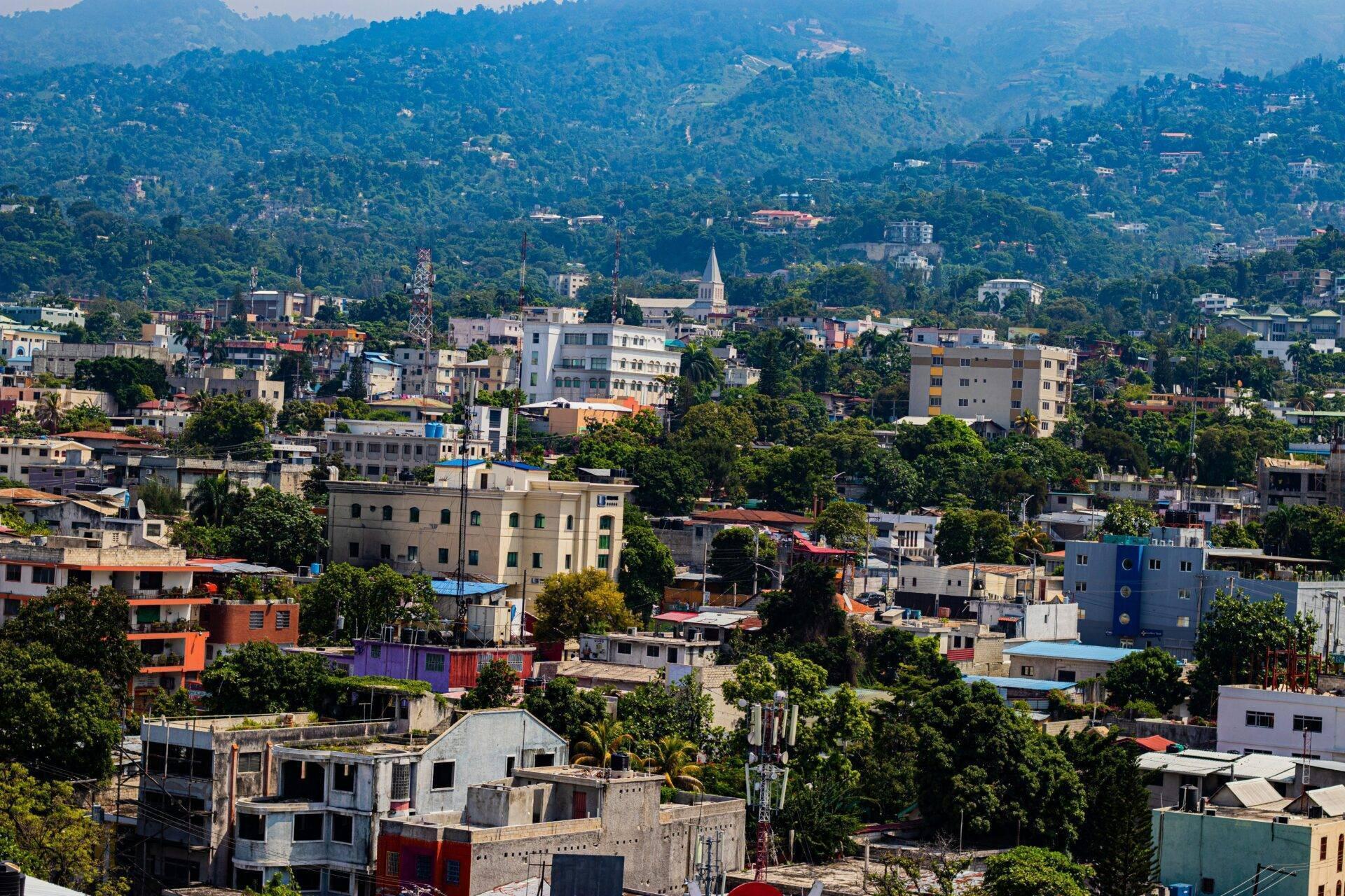 Vue aérienne d’une ville montagneuse tropicale avec bâtiments colorés, végétation dense et église blanche au centre