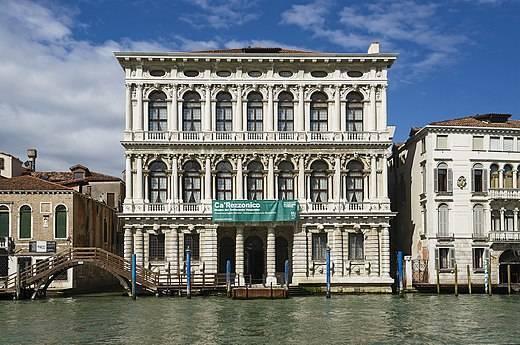Un palais vénitien blanc aux façades ornées surplombe le Grand Canal sous un ciel bleu dégagé