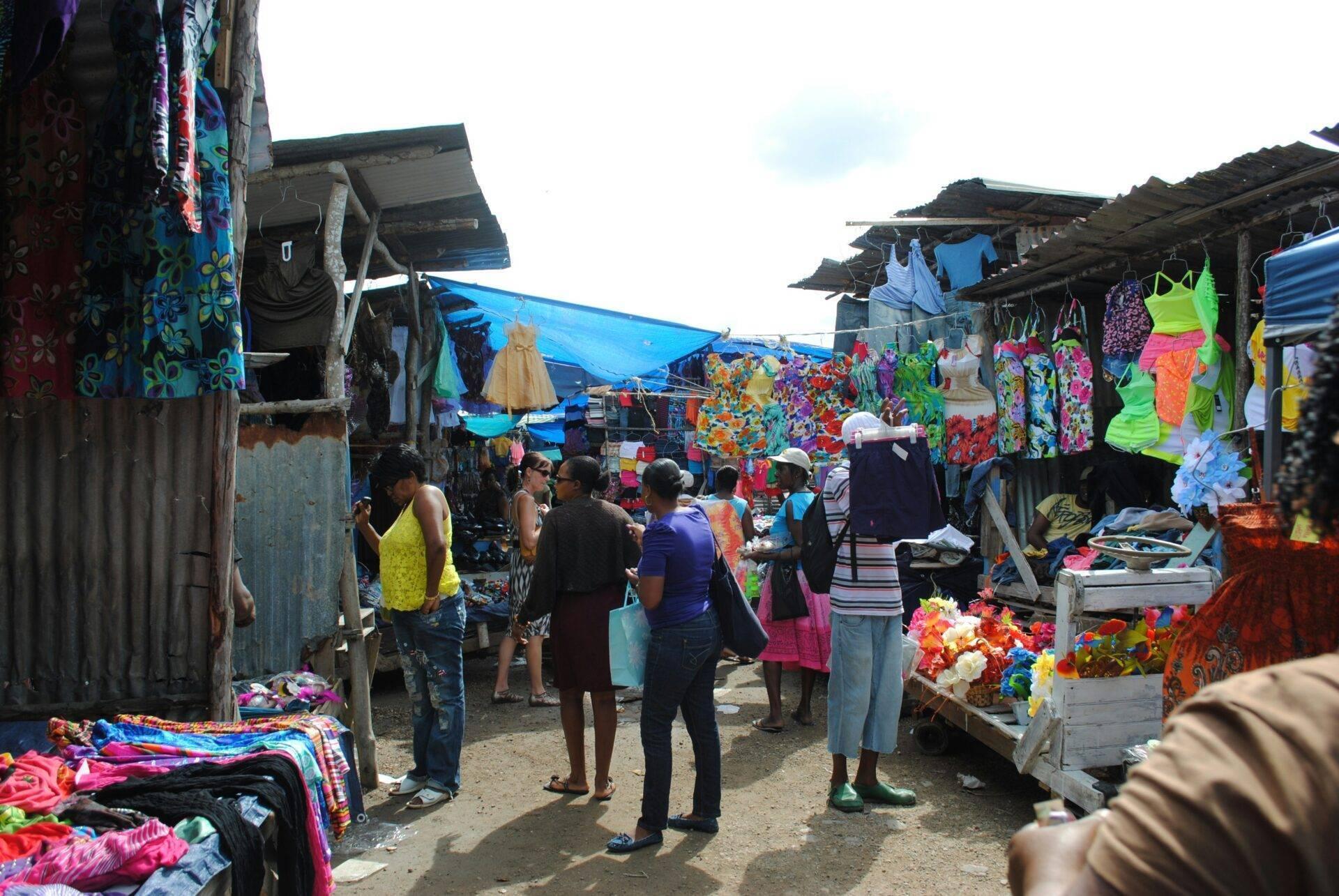 Un marché coloré en plein air avec des vêtements et textiles vibrants exposés, des visiteurs qui flânent parmi les étals