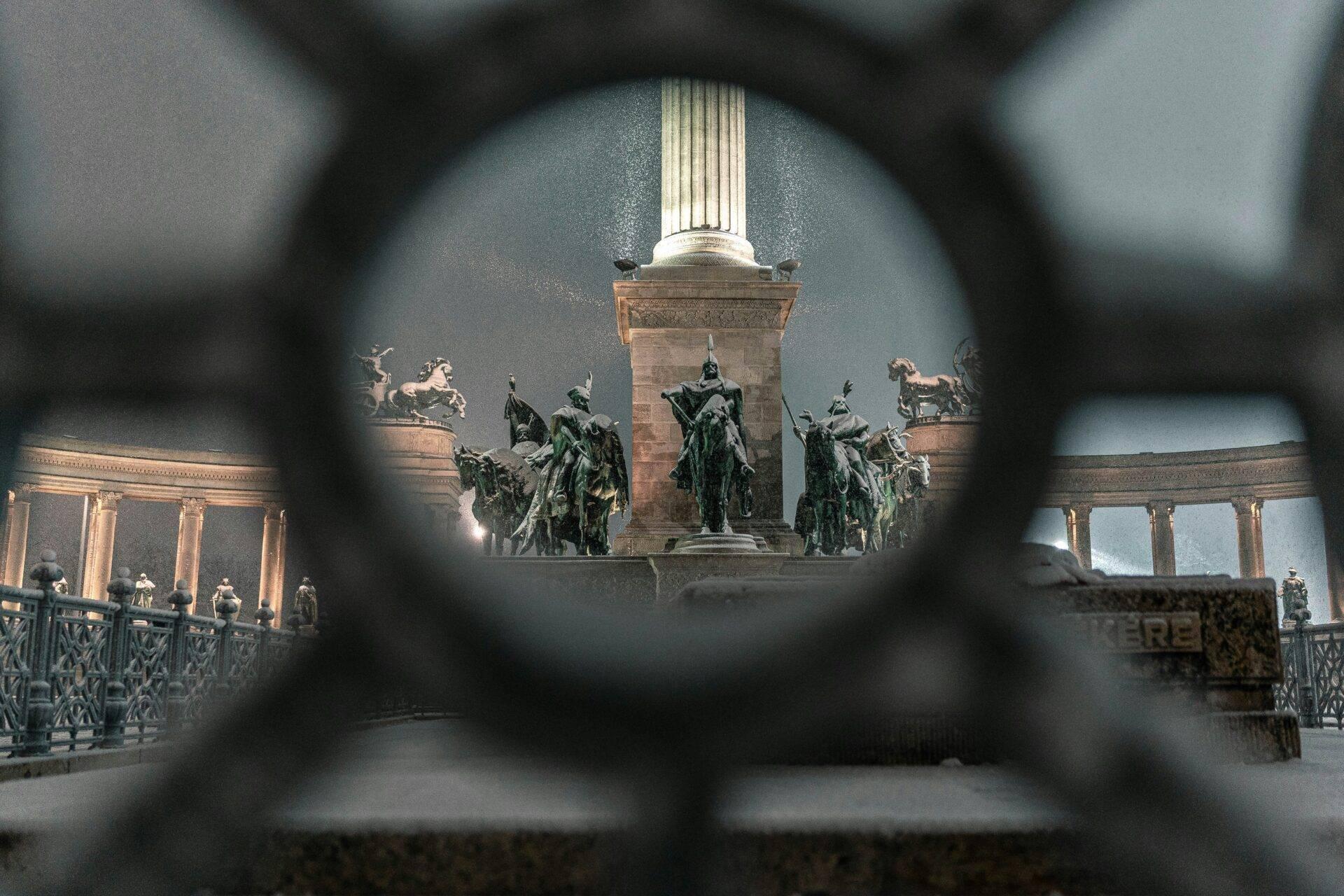 Vue à travers une grille de fer du monument aux héros avec statues équestres et colonnade à Budapest