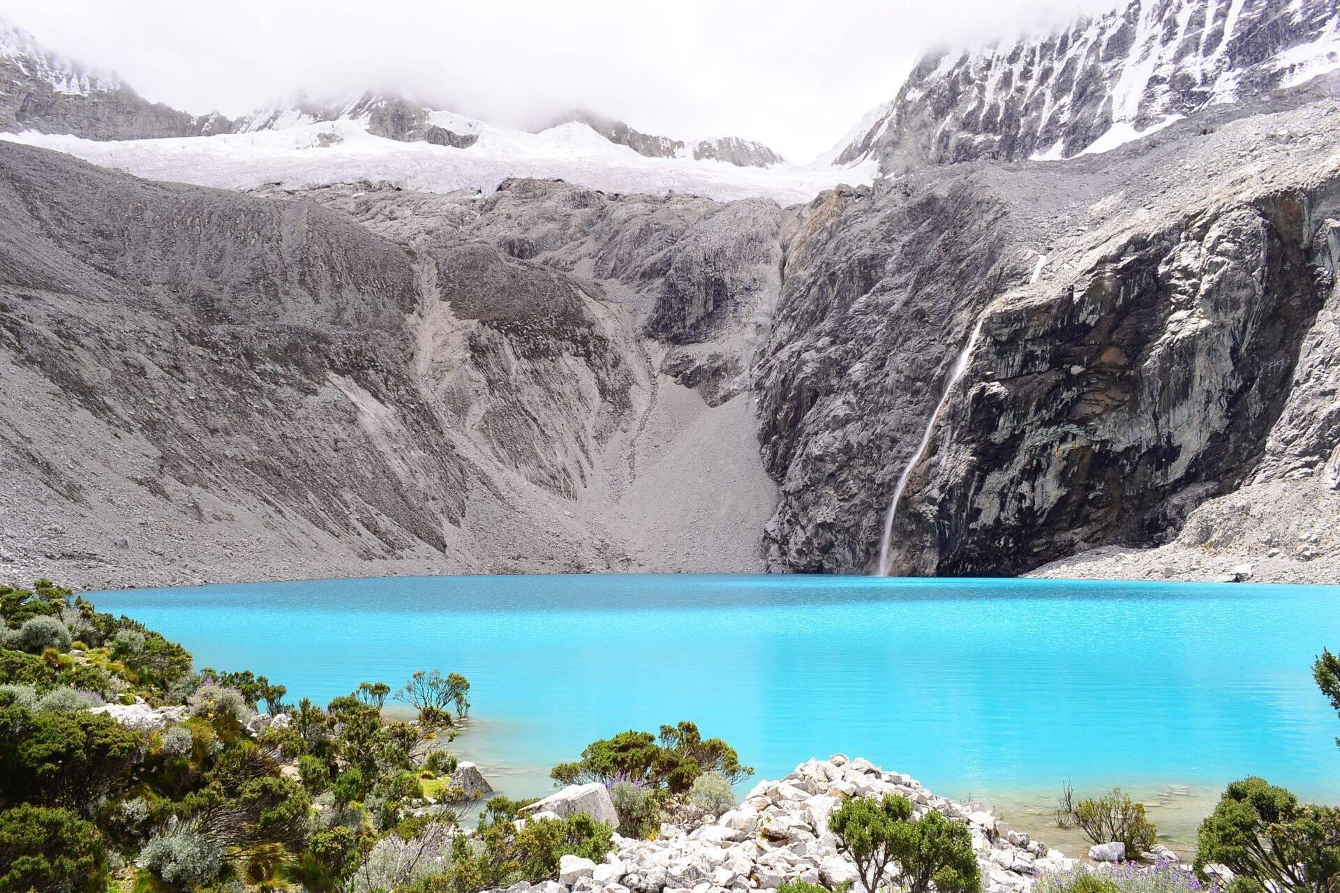 Lac de montagne d’un bleu turquoise intense entouré de pics enneigés, glacier et cascade dans un décor alpin