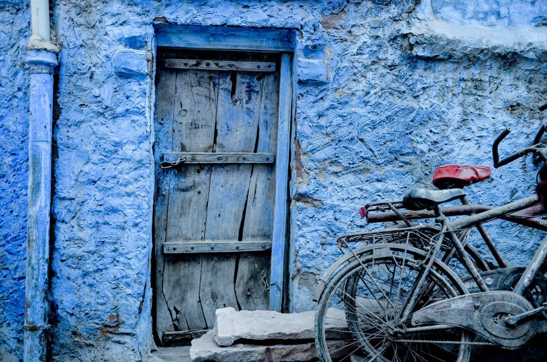 Porte en bois bleu sur un mur peint d’une vieille ville avec un vélo rouillé appuyé contre le mur