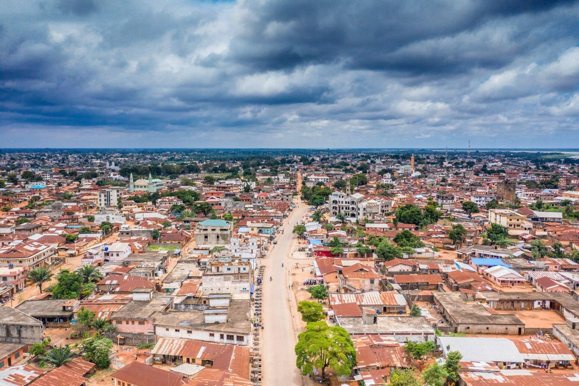 Vue aérienne d’une ville africaine avec bâtiments colorés, toits rouges et une rue principale sous ciel nuageux