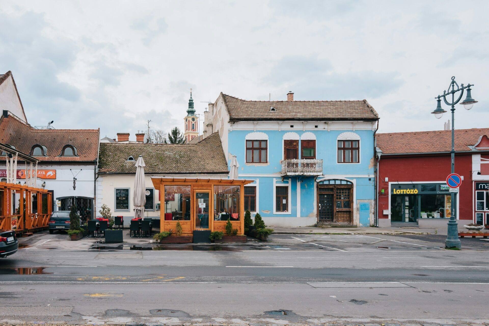 Une place de village d’Europe centrale avec maisons colorées aux façades bleues et blanches, église en arrière-plan