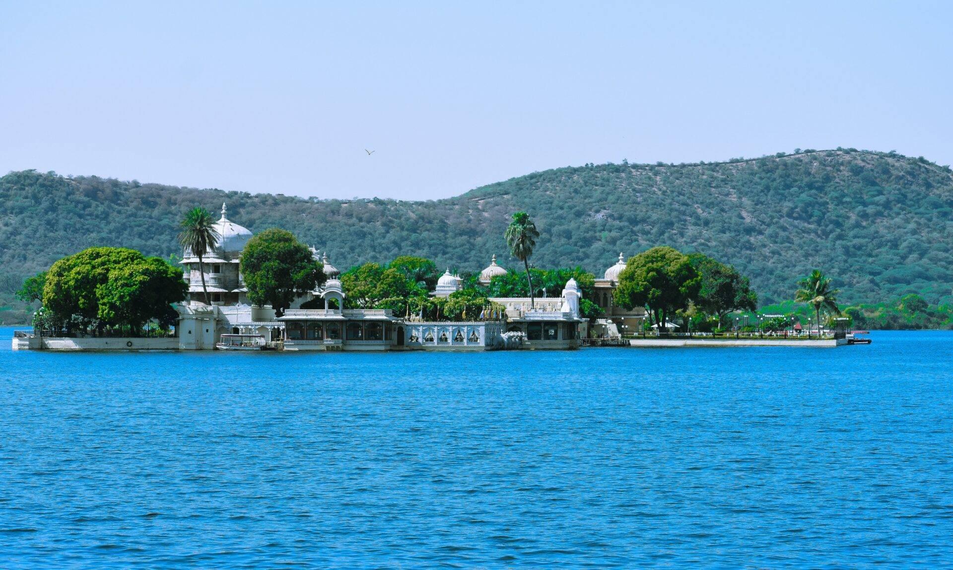 Un temple blanc avec dômes situé sur les rives d’un lac bleu, entouré de verdure et de collines boisées