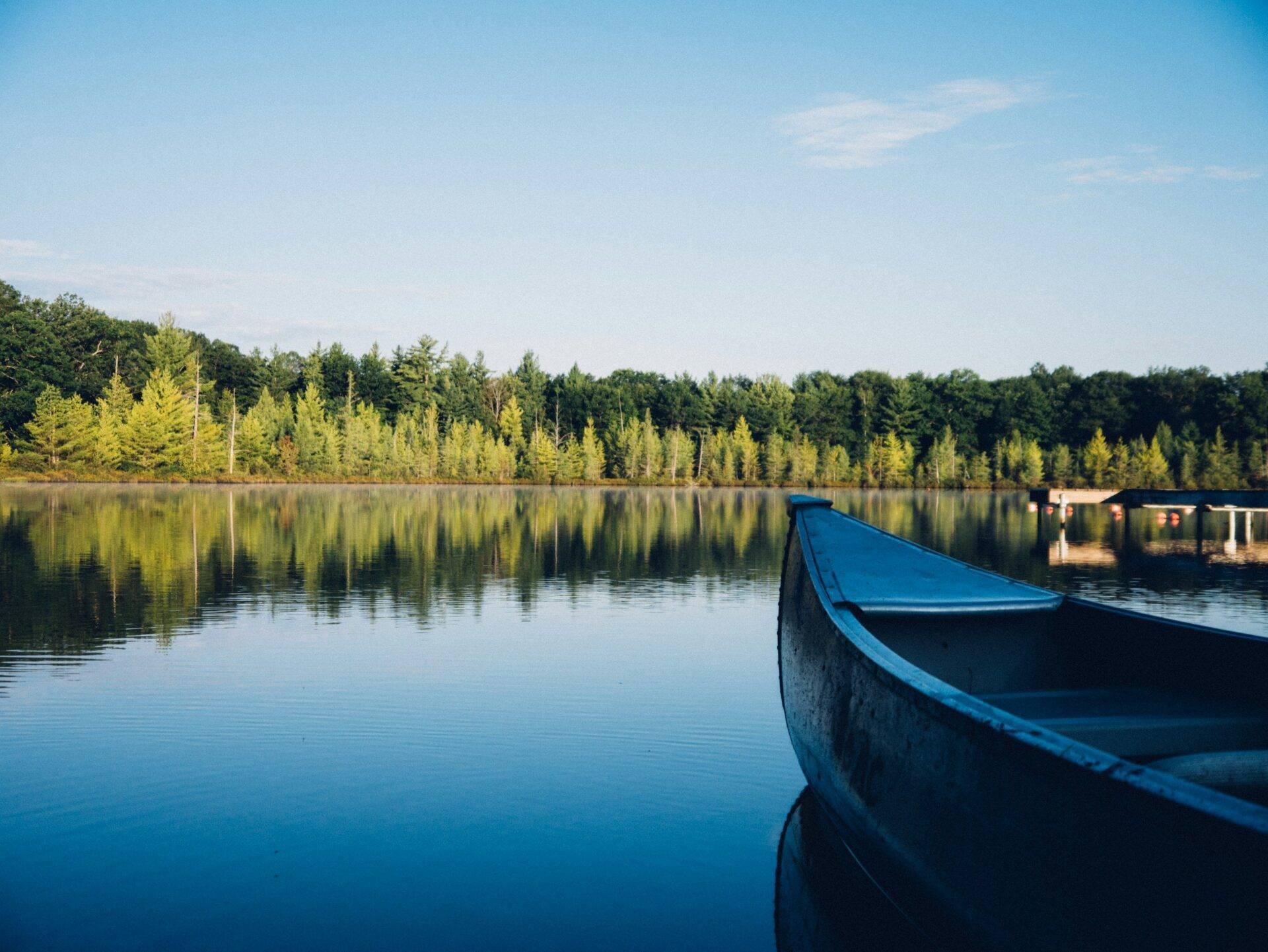 Un bateau bleu amarré sur un lac calme bordé de forêts de conifères verdoyantes sous un ciel dégagé