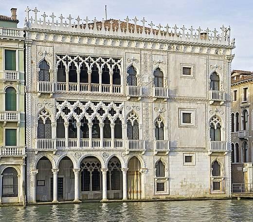 Façade gothique vénitienne en marbre blanc et rose avec arcades ogivales reflétées dans l’eau du canal